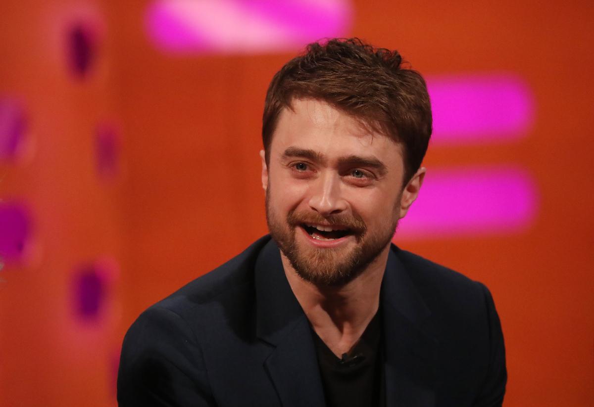 Daniel Radcliffe, star of the Harry Potter movies, laughing with a red background