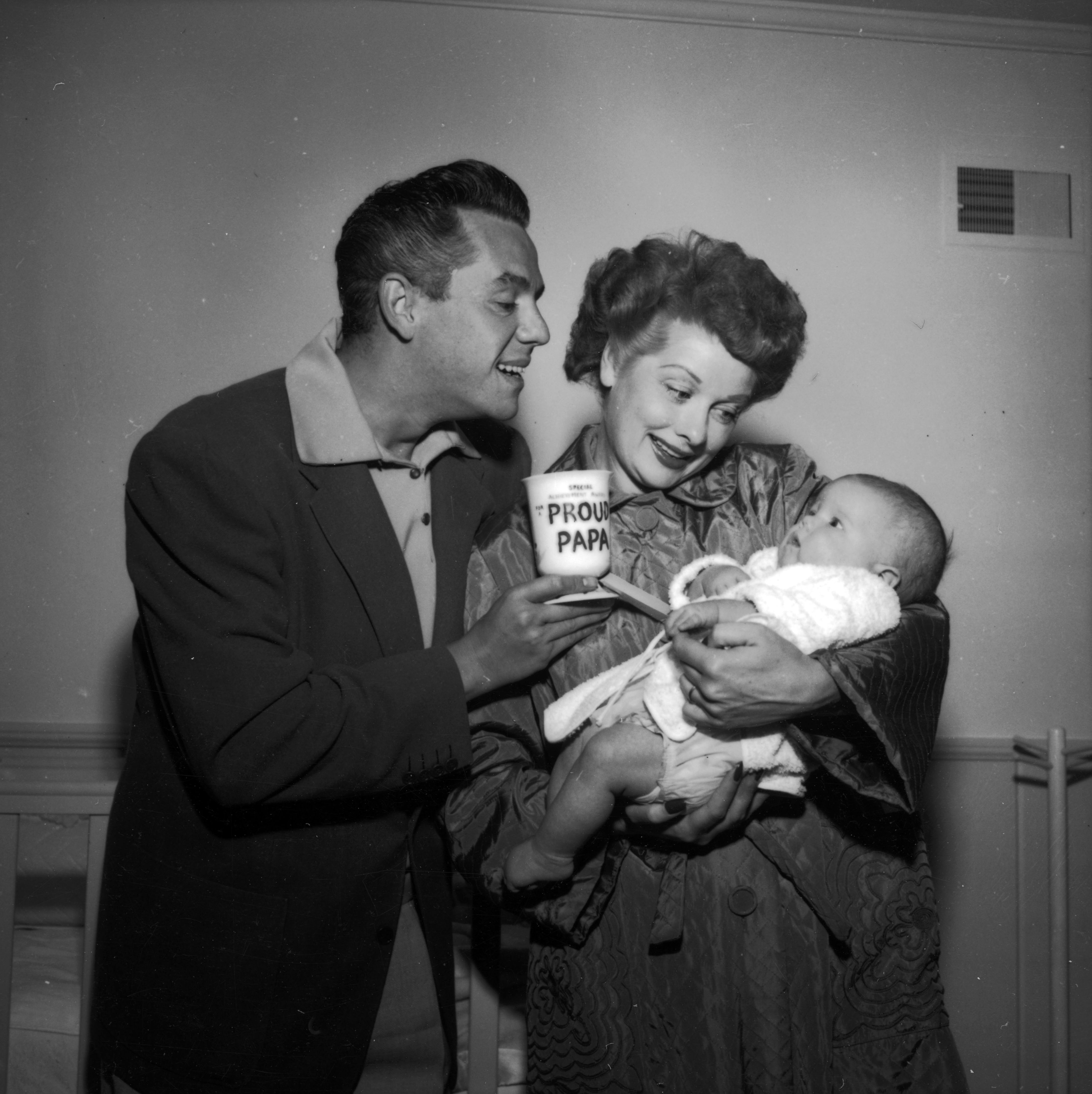 Lucille Ball at home with her husband Desi Arnaz and their son Desi Jr., 1953. Desi Sr. is holding a mug with the caption 'Proud Papa' on it.