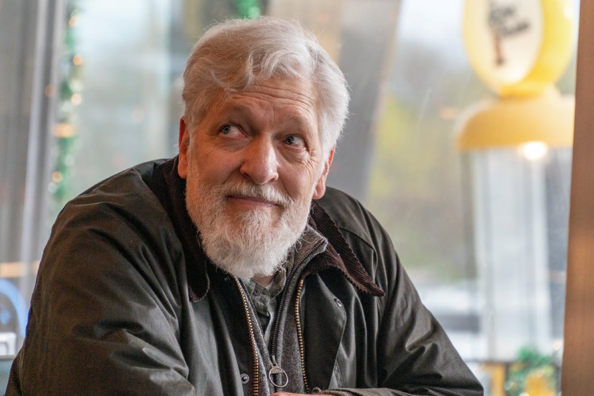 Clancy Brown as Kurt in Dexter: New Blood Episode 7. Kurt sits at a table at the diner and smiles, looking up at something.