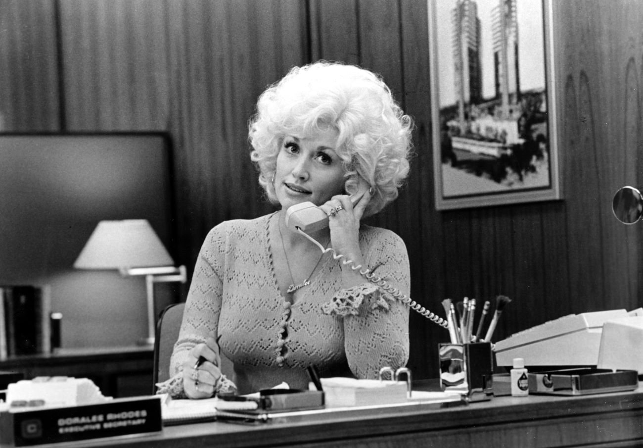 A black and white photo of Dolly Parton sitting at a desk on the phone for 9 to 5.