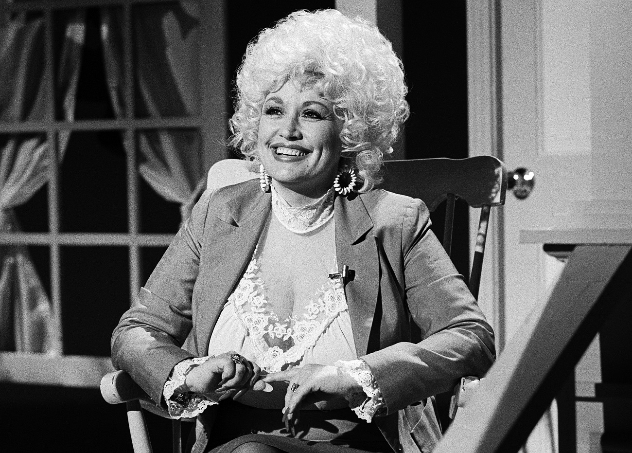 A black and white photo of Dolly Parton wearing a white lace top and blazer. She is at the premier of The Best Little Whorehouse in Texas.
