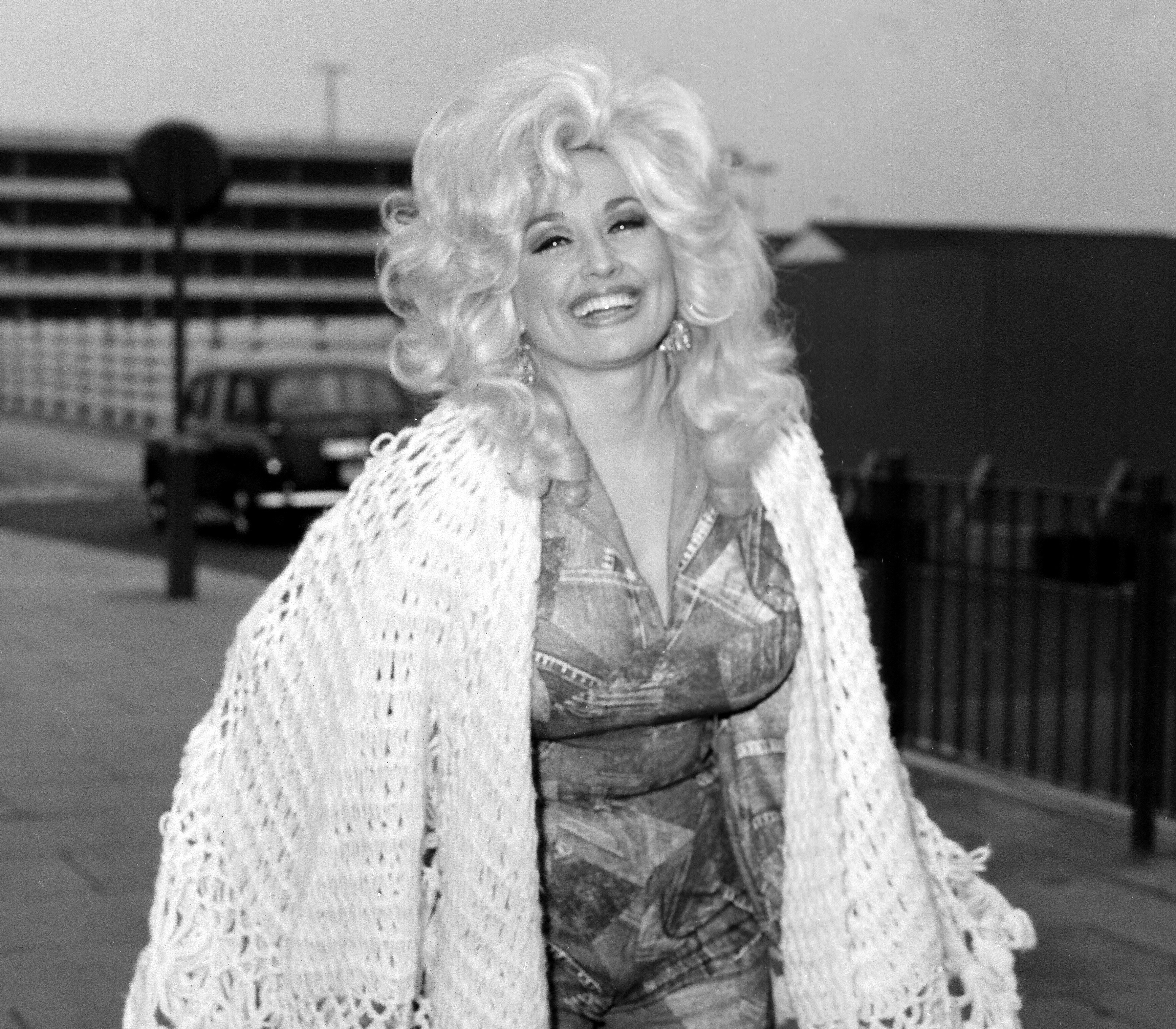 A black and white picture of a young Dolly Parton in a jumpsuit with a white knit blanket.