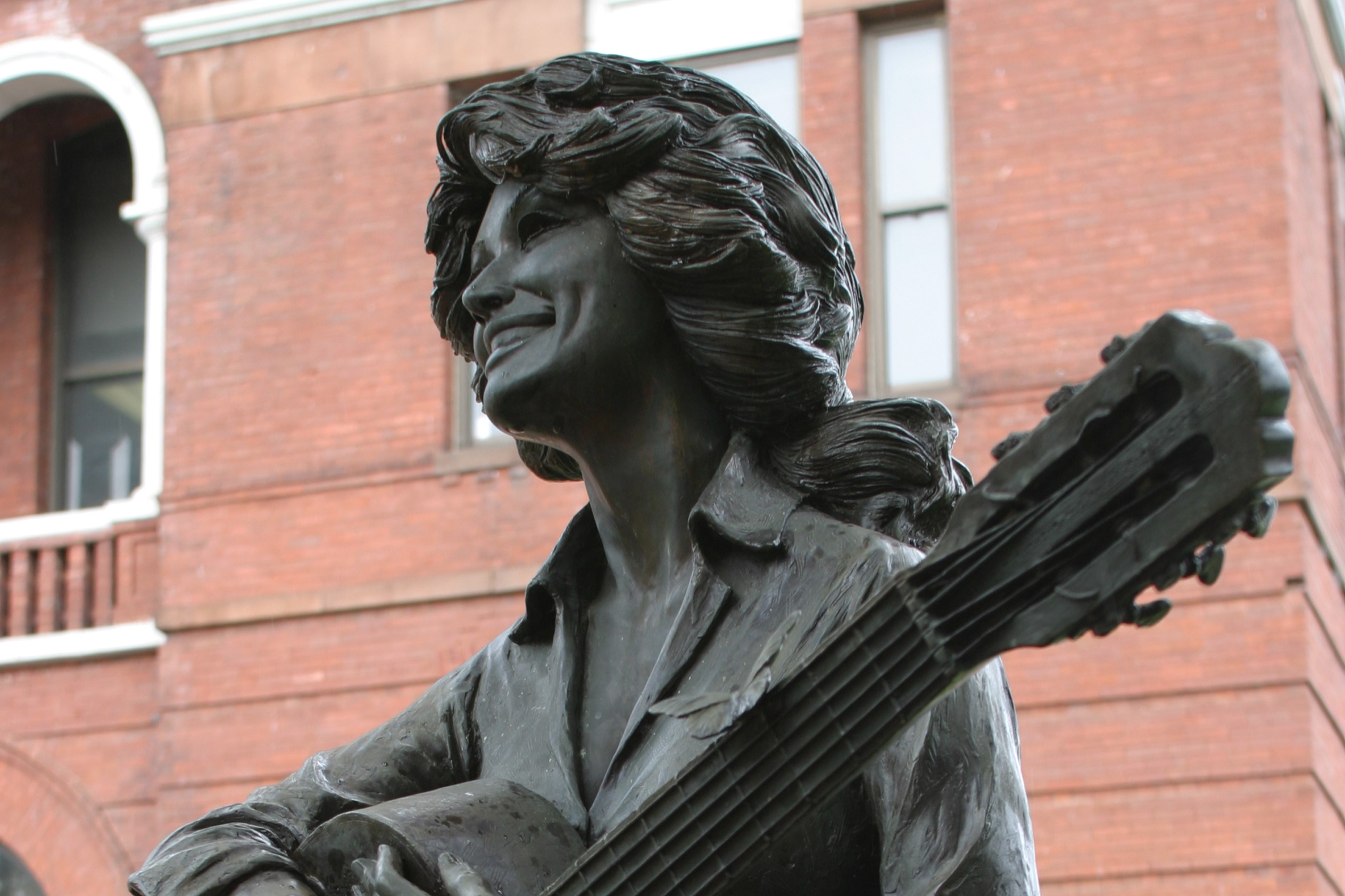 A statue of Dolly Parton holding a guitar outside of a brick building.