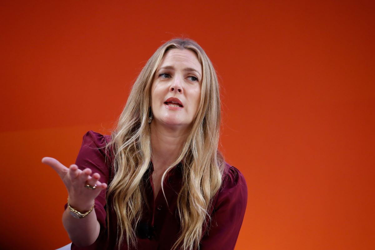 Drew Barrymore in a maroon shirt, holding one hand out in front of her