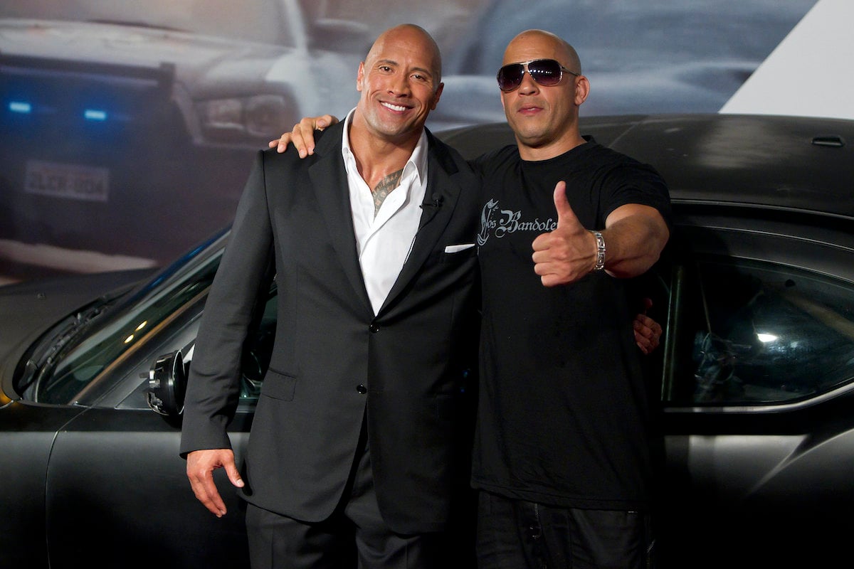 Dwayne Johnson wears a suit and smiles while Vin Diesel wears sunglasses and gives a thumbs-up during the ‘Fast Five’ premiere