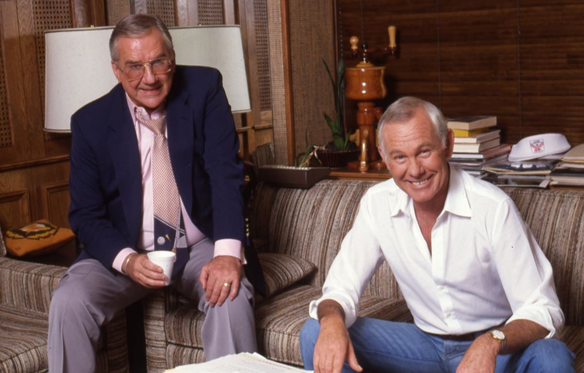 Ed McMahon in a pink shirt and tie with a dark blue jacket and Johnny Carson in a white button down shirt, both sitting on a couch c. 1985 