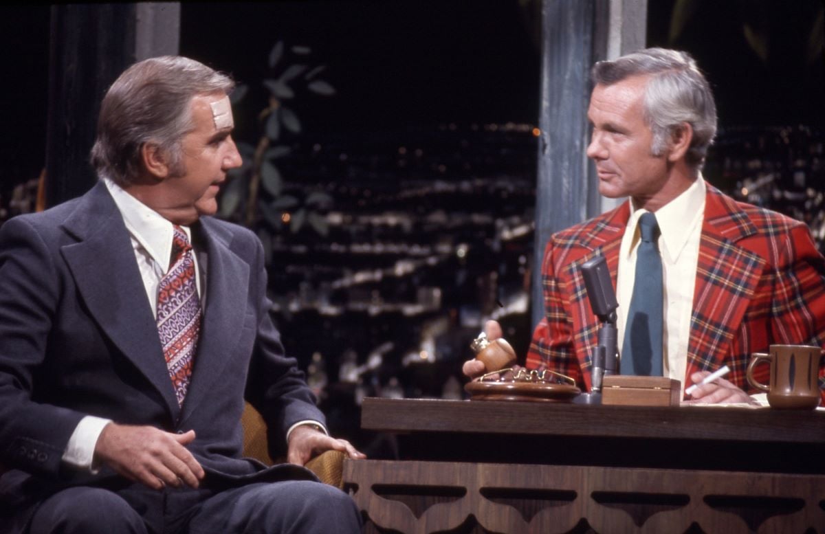 Ed McMahon, in a gray suit and striped tie, sits next to Johnny Carson, in a plaid jacket