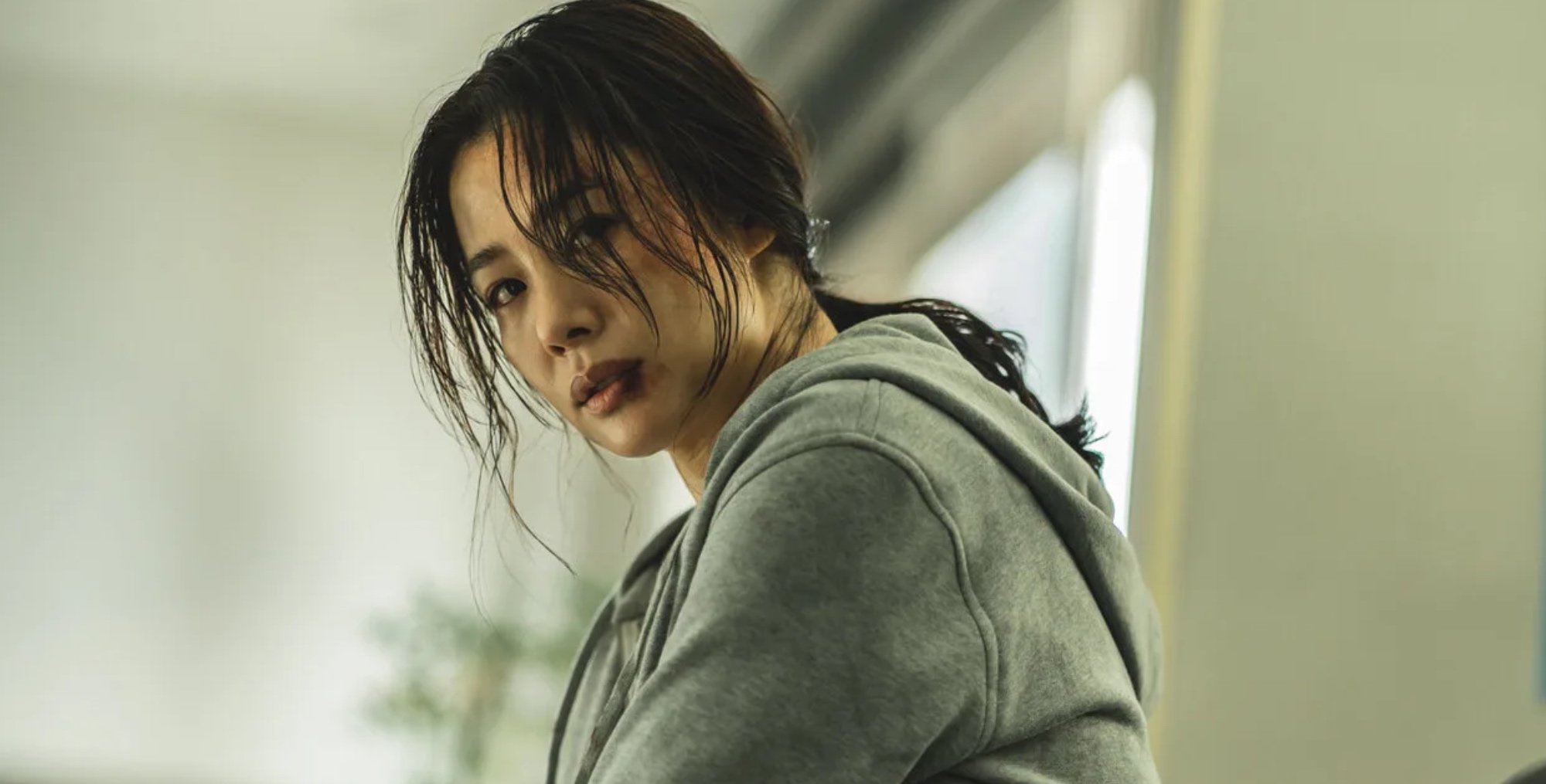 Female lead Han Hye-jin from 'Hellbound' K-drama wearing red sweater and bruised face.