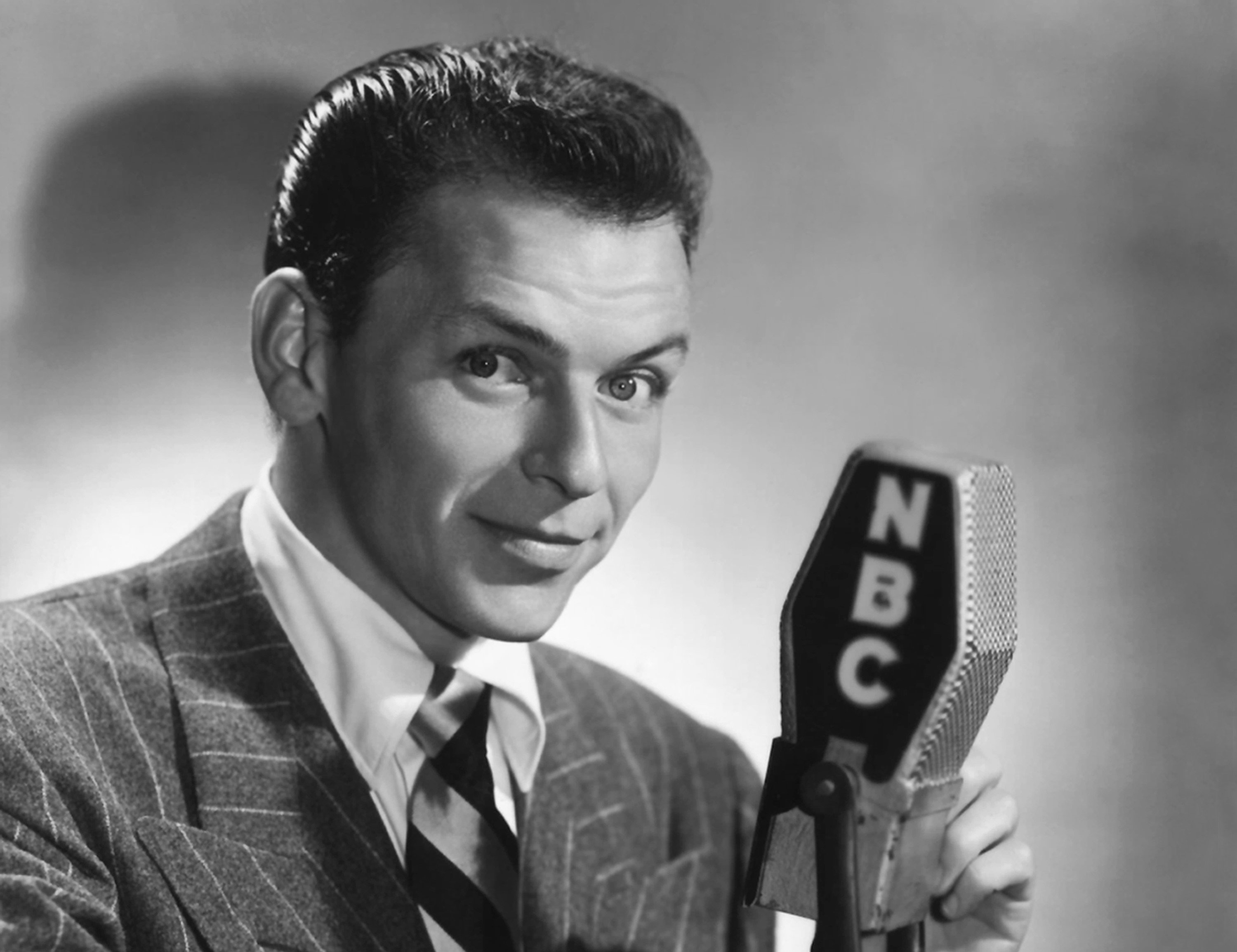 Frank Sinatra wears a suit and holds an NBC microphone.