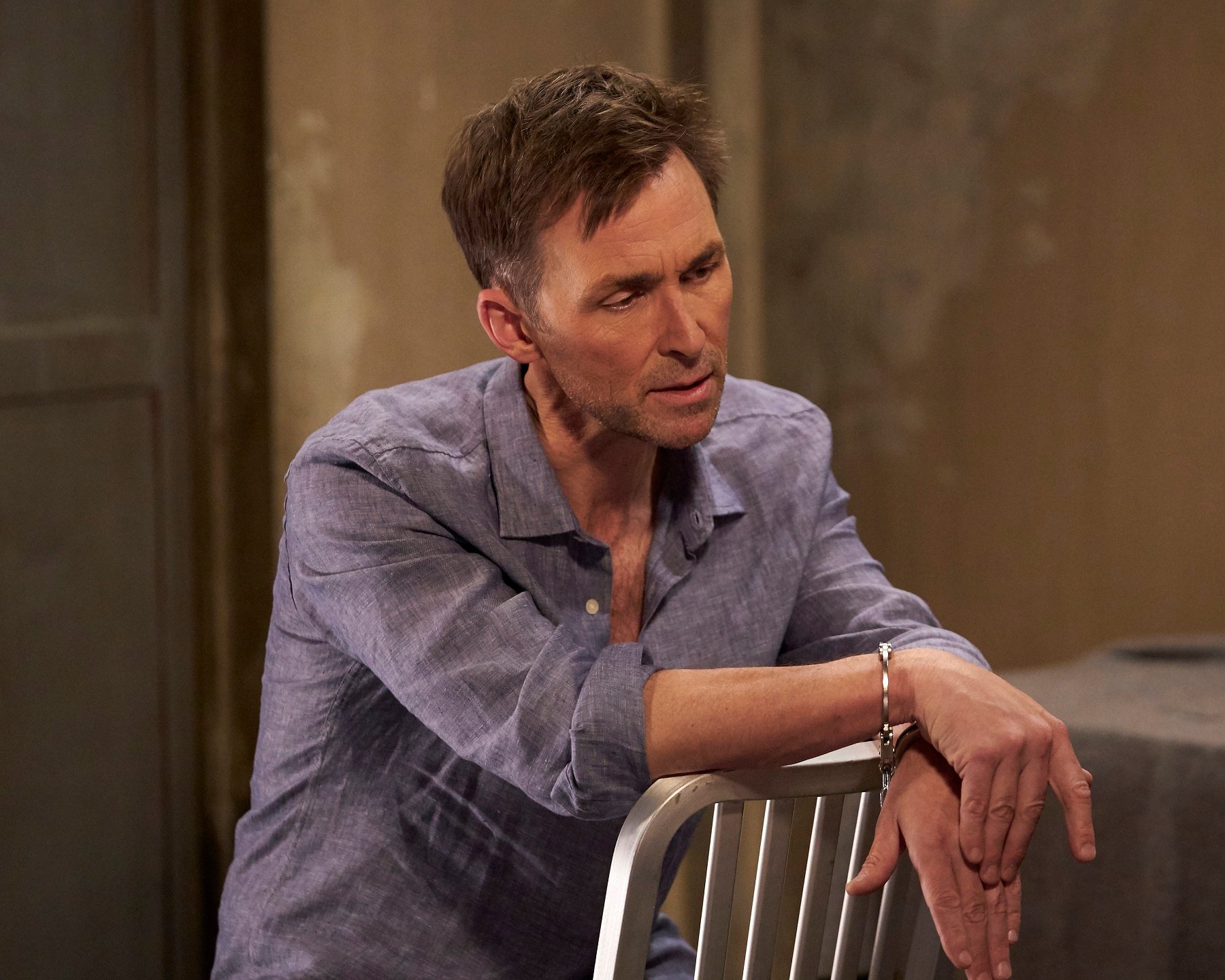 General Hospital star James Patrick Stuart is pictured handcuffed, sitting on a chair, and dressed in blue