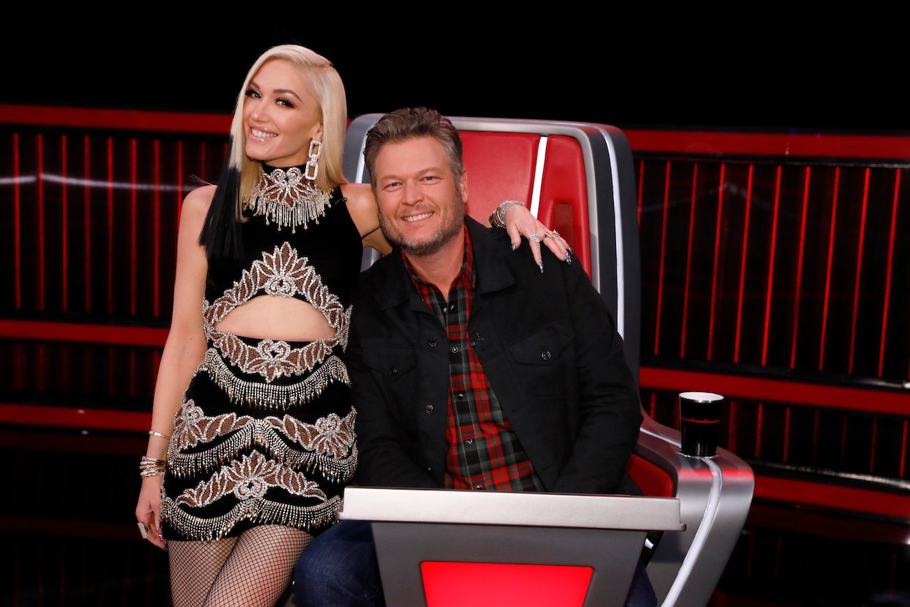 Gwen Stefani standing next to Blake Shelton, who is seated in a chair