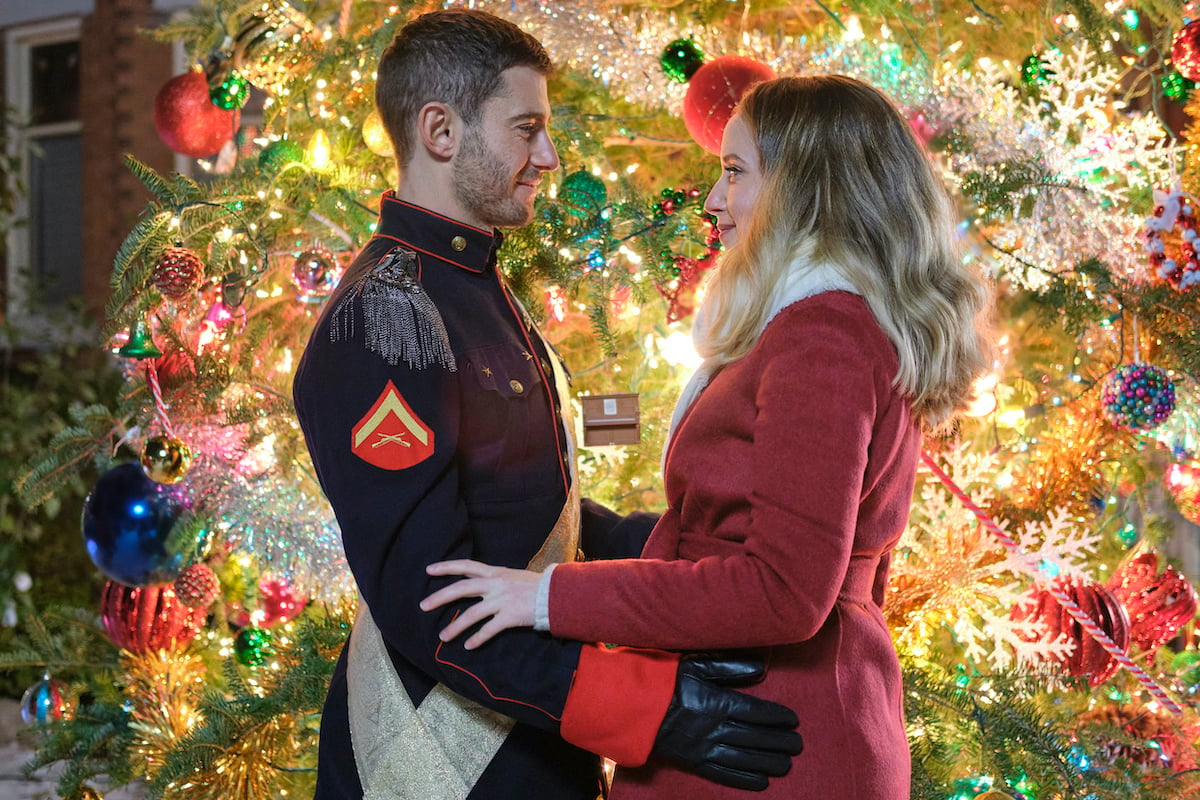 Julian Morris and Megan Park in front of a Christmas tree in Hallmark's 'A Royal Queens Christmas'