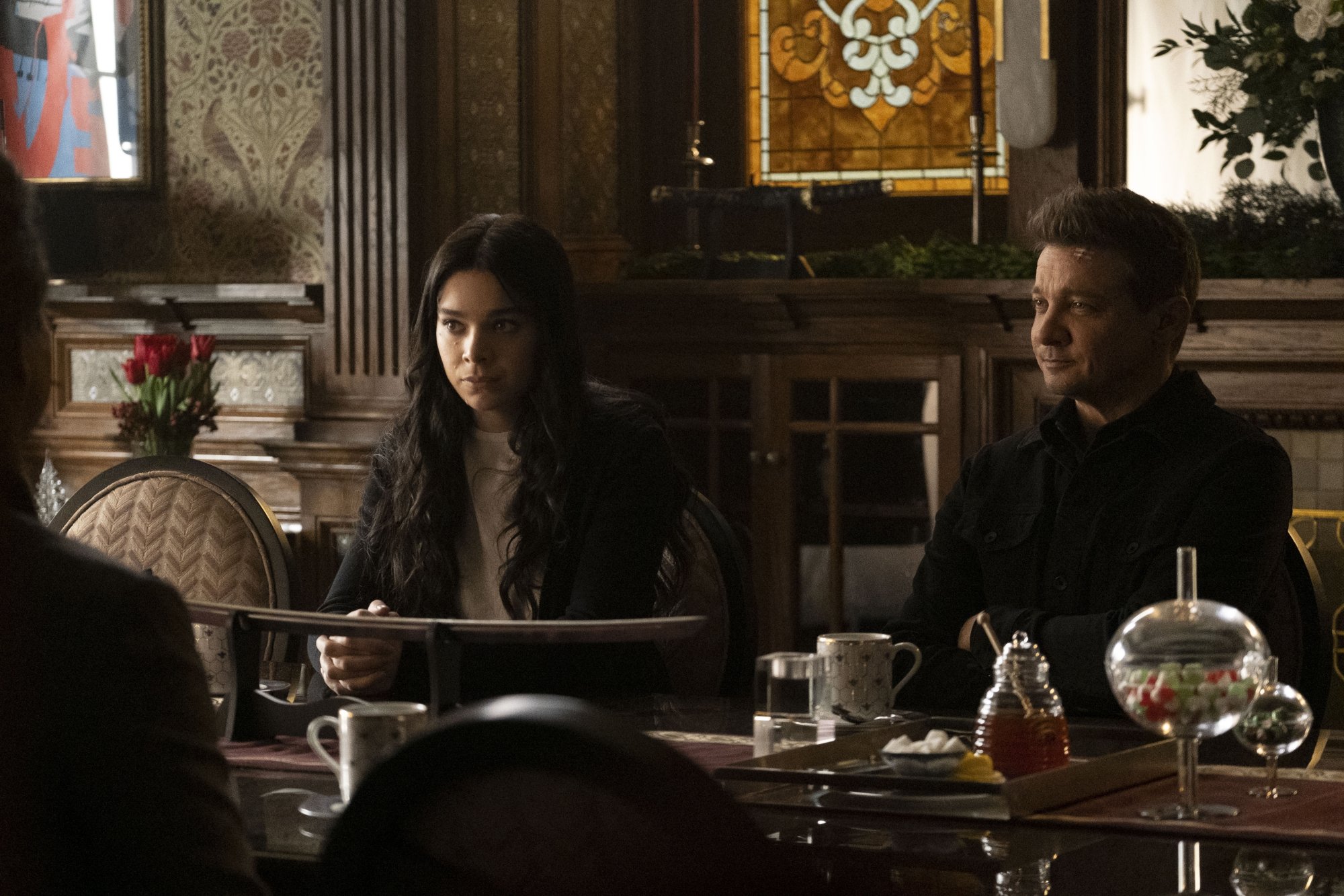 Hailee Steinfeld and Jeremy Renner as Kate Bishop and Clint Barton in 'Hawkeye' Episode 4 on Disney+. They're sitting at a table speaking to Kate's mom and step-father.
