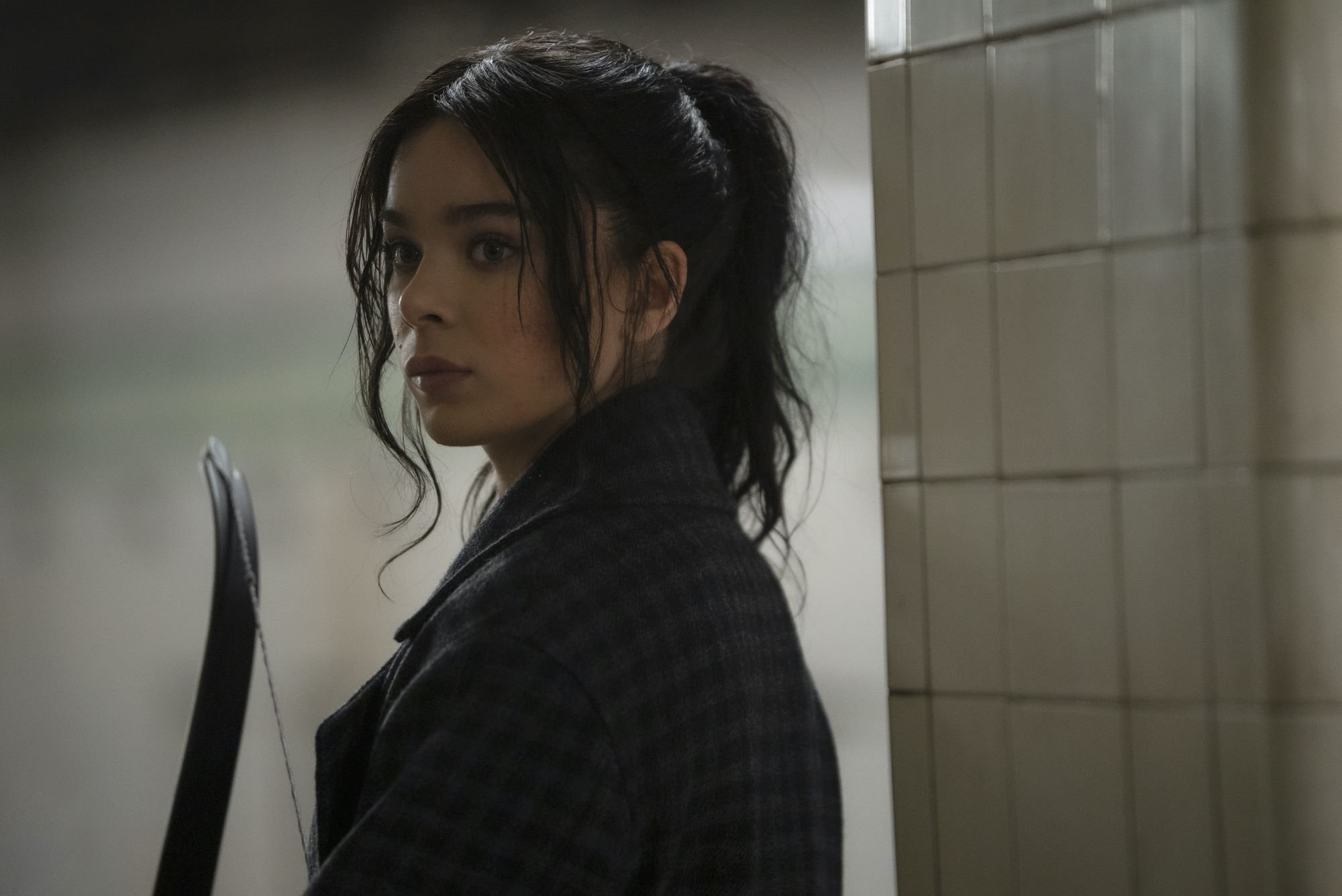 'Hawkeye' Episode 5 star Hailee Steinfeld, in character as Kate Bishop, wears a gray plaid coat and holds a bow. Kingpin appears in 'Hawkeye' Episode 5.