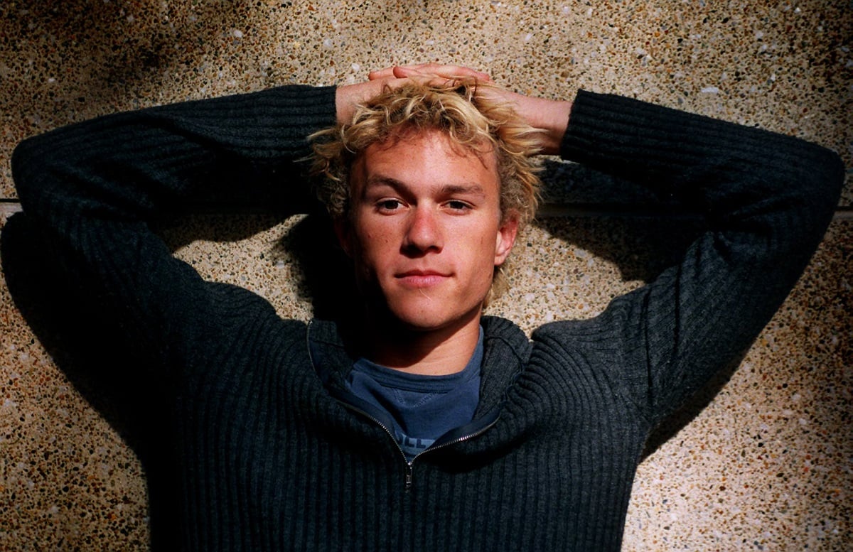 Heath Ledger smirking at the camera while wearing a blue sweater.