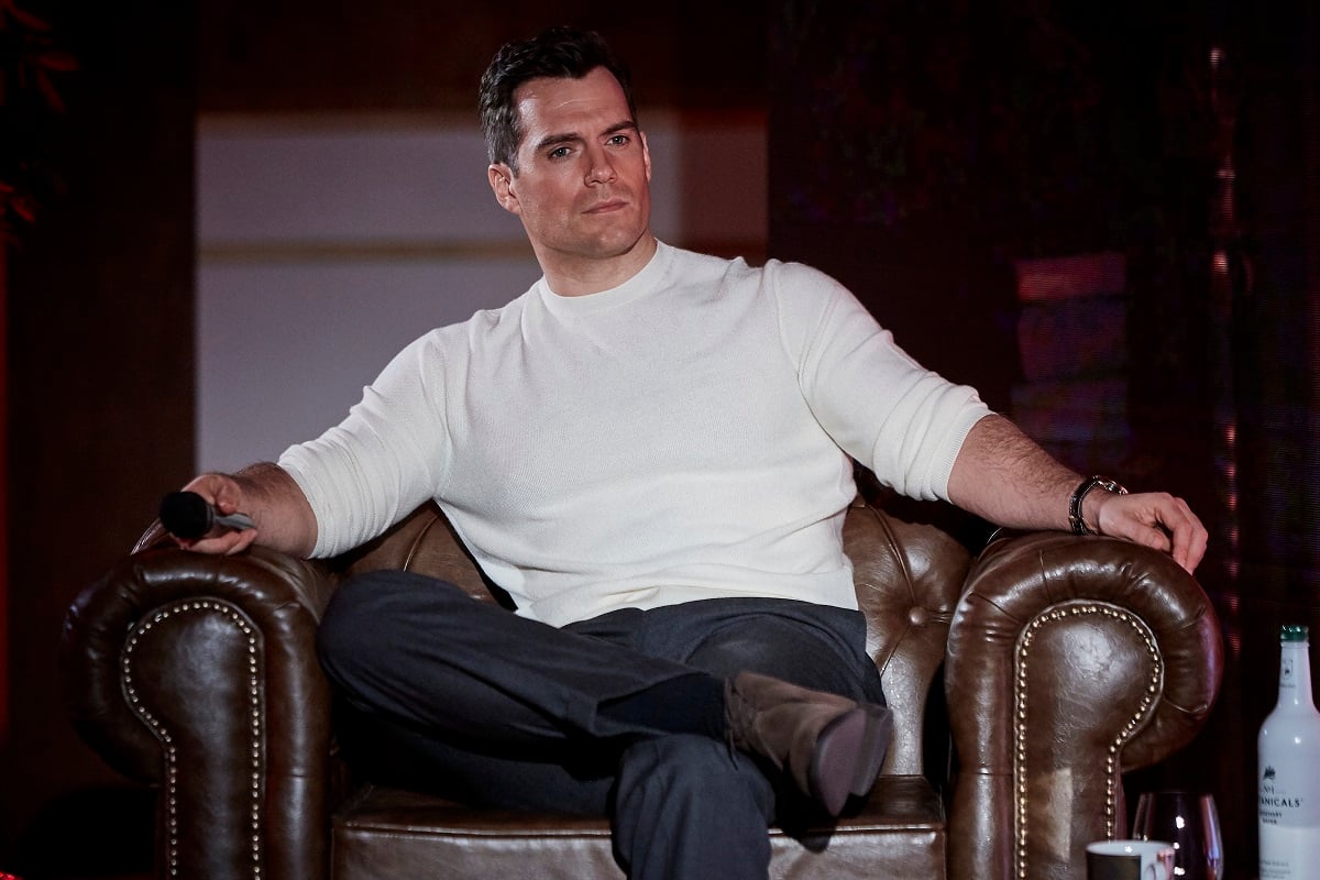 Henry Cavill sitting down while wearing a white shirt.