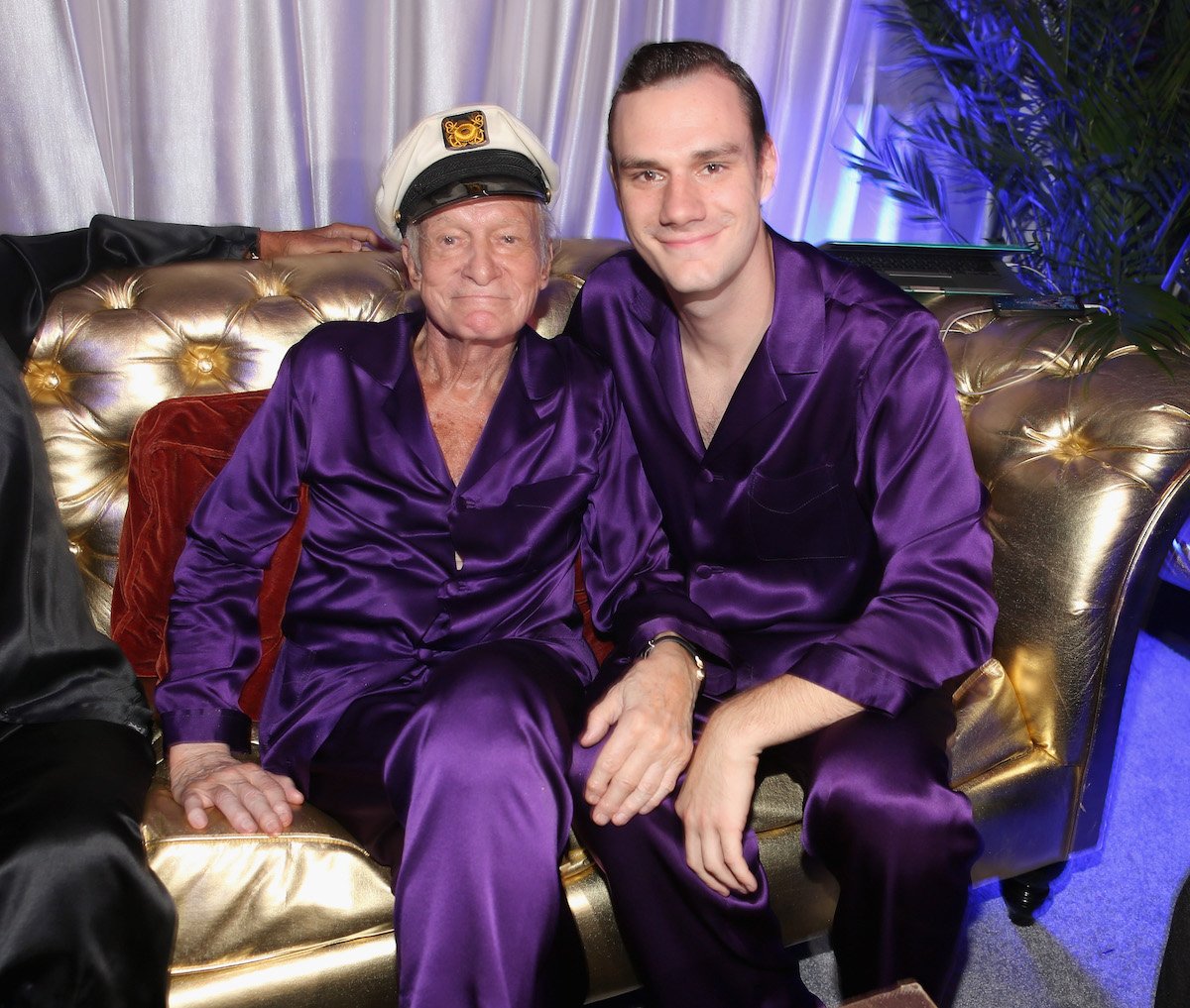 Playboy founder Hugh Hefner and his son Cooper Hefner sit on a couch during a Playboy Mansion party in 2014