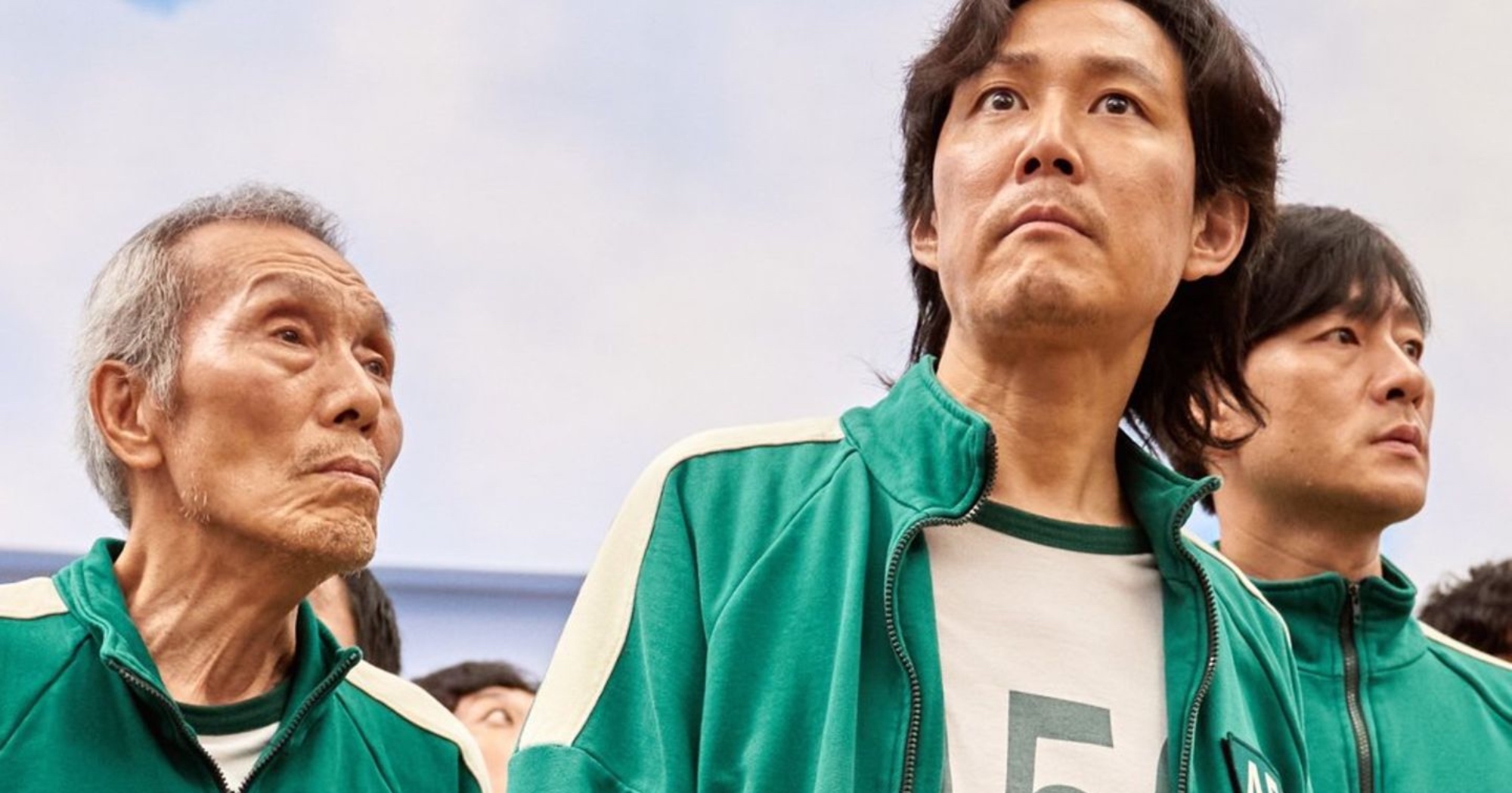 Il-nam and Gi-hun from 'Squid Game' theory wearing green jumpsuits on playground.