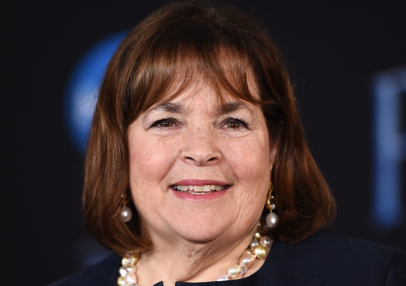 Ina Garten smiles as she looks on wearing a black top and pearl necklace