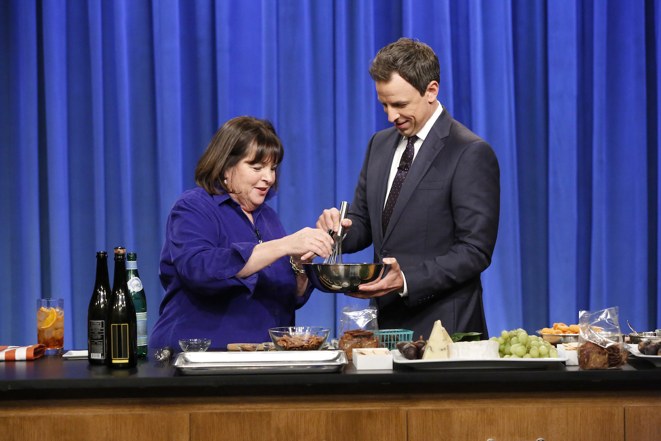Seth Meyers whisks ingredients in a bowl as Ina Garten pours in another ingredient