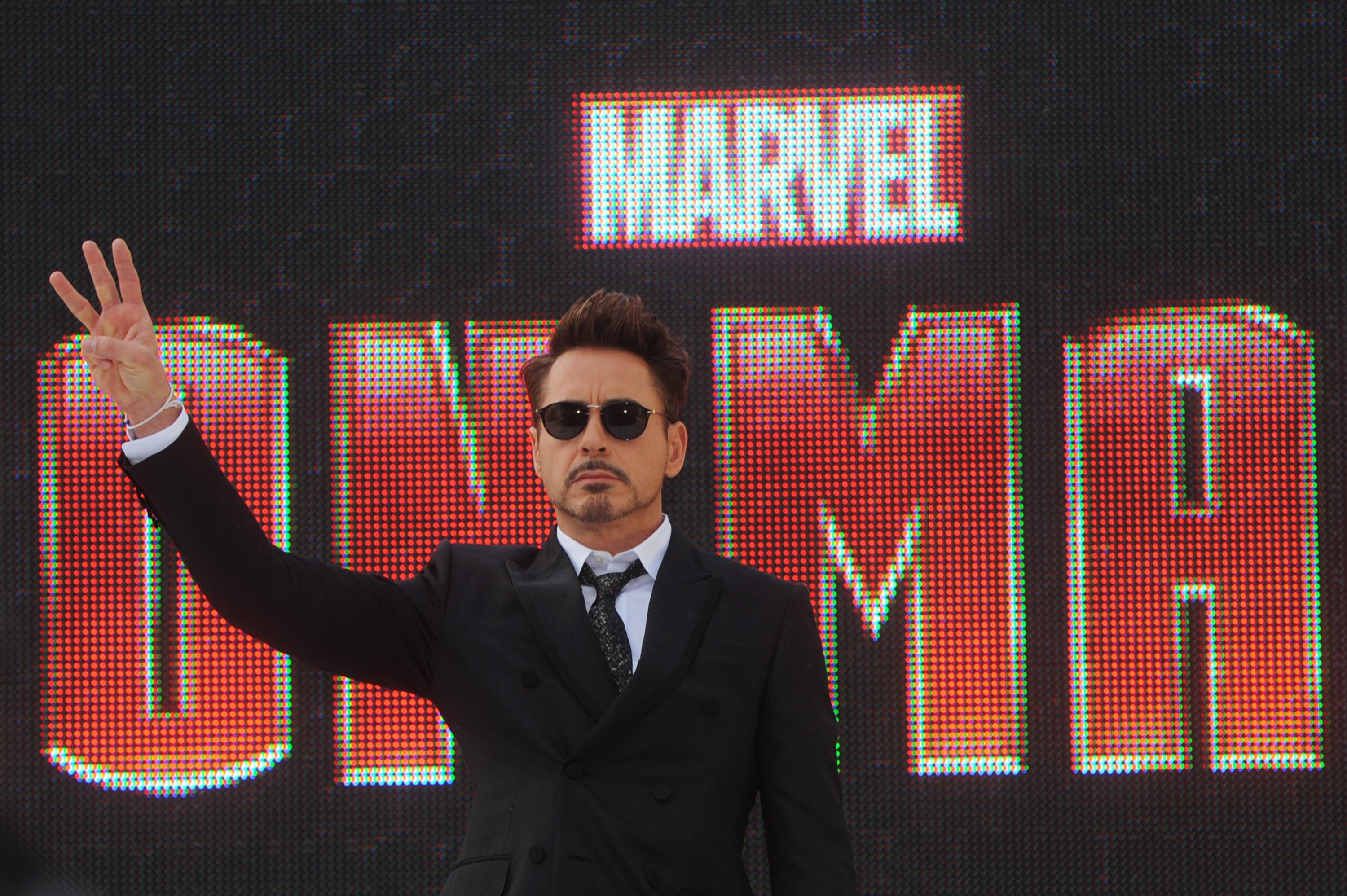 'Iron Man 3' star Robert Downey Jr. stands in front of a sign for the movie and wears a black suit jacket over a white button-up shirt and black tie and wears black sunglasses. Is 'Iron Man 3' a Christmas movie?