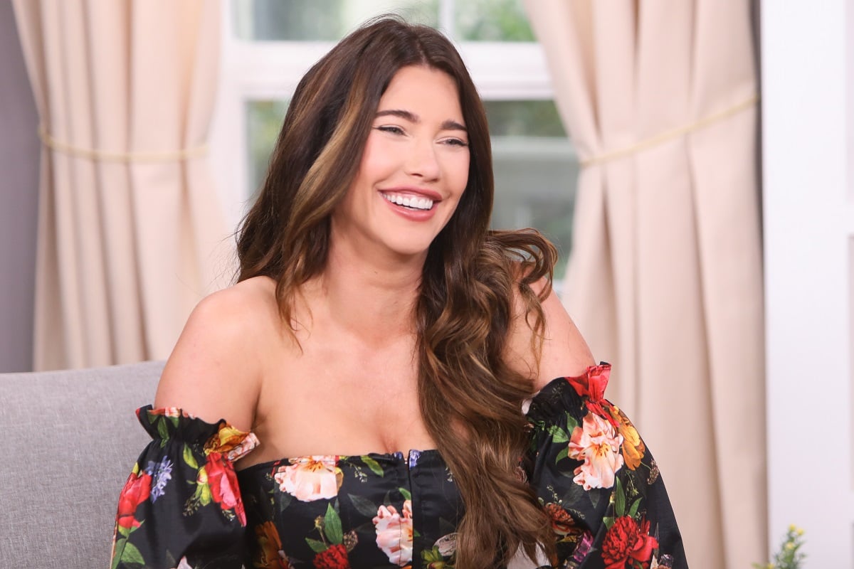 'The Bold and the Beautiful' actor Jacqueline MacInnes Wood wearing a black floral blouse, and sitting in a living room set.
