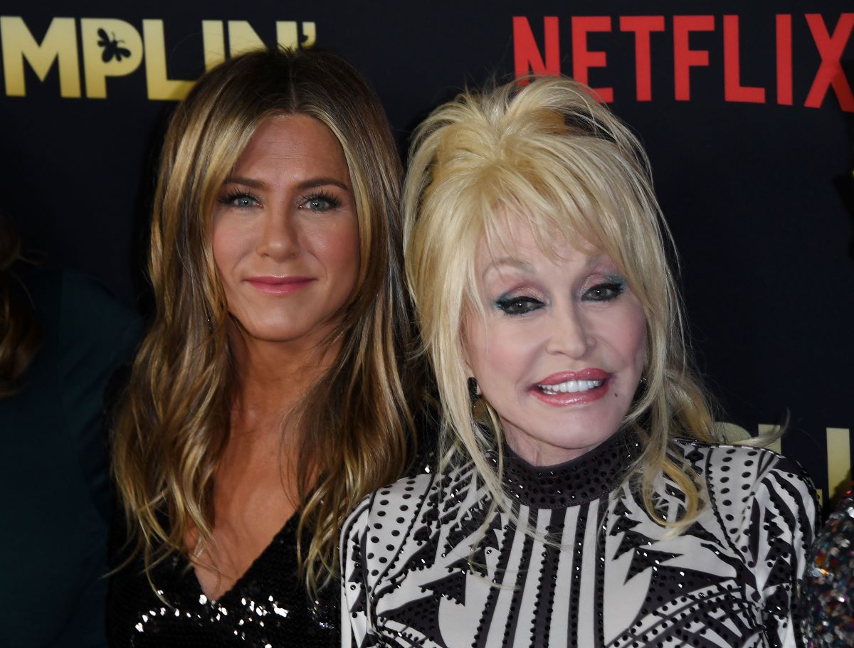 Jennifer Aniston in a black shirt, standing beside a smiling Dolly Parton dressed in black and white