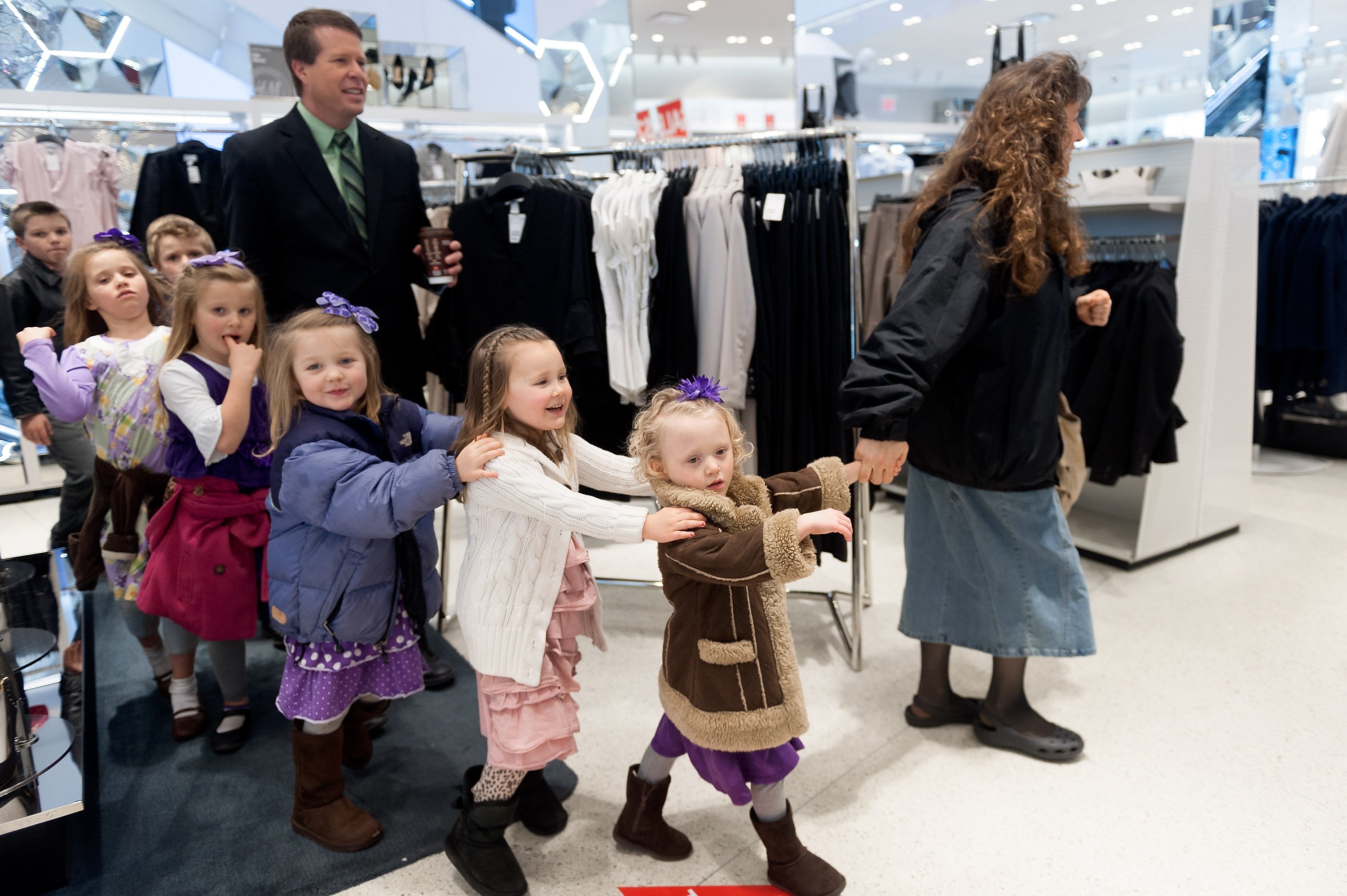 Michelle Duggar and Jim Bob Duggar escort a line of their children through a store