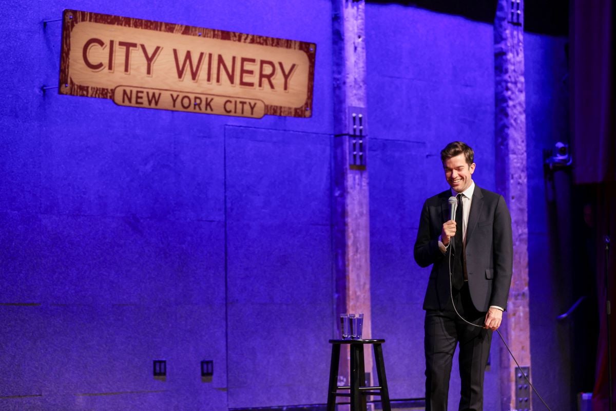 John Mulaney in a suit and tie, holding a microphone