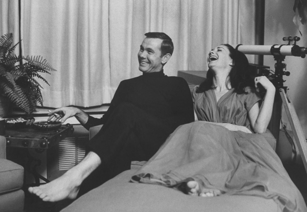 Johnny Carson in black, seated next to second wife, Joanne Carson, who is laughing