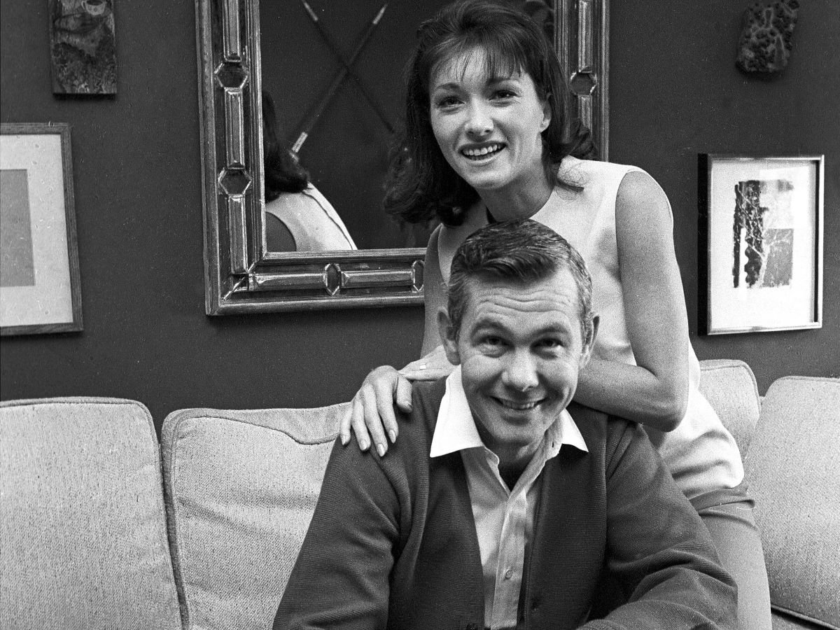 Joanne Carson leans on the back of Johnny Carson, both smiling