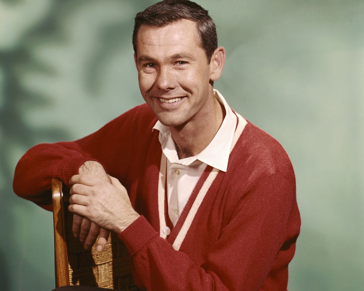 Johnny Carson smiles in a red cardigan and white button down shirt