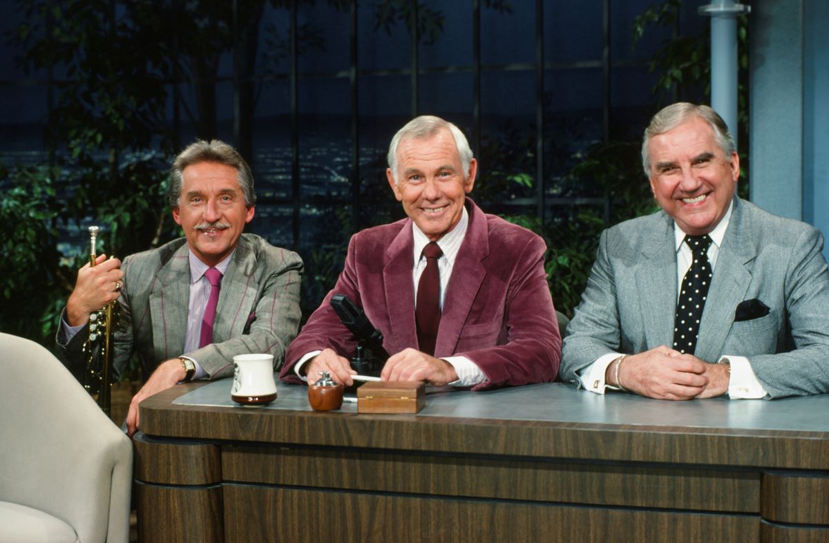 Bandleader Doc Severinsen, host Johnny Carson, and announcer Ed McMahon sit at 'The Tonight Show' desk.