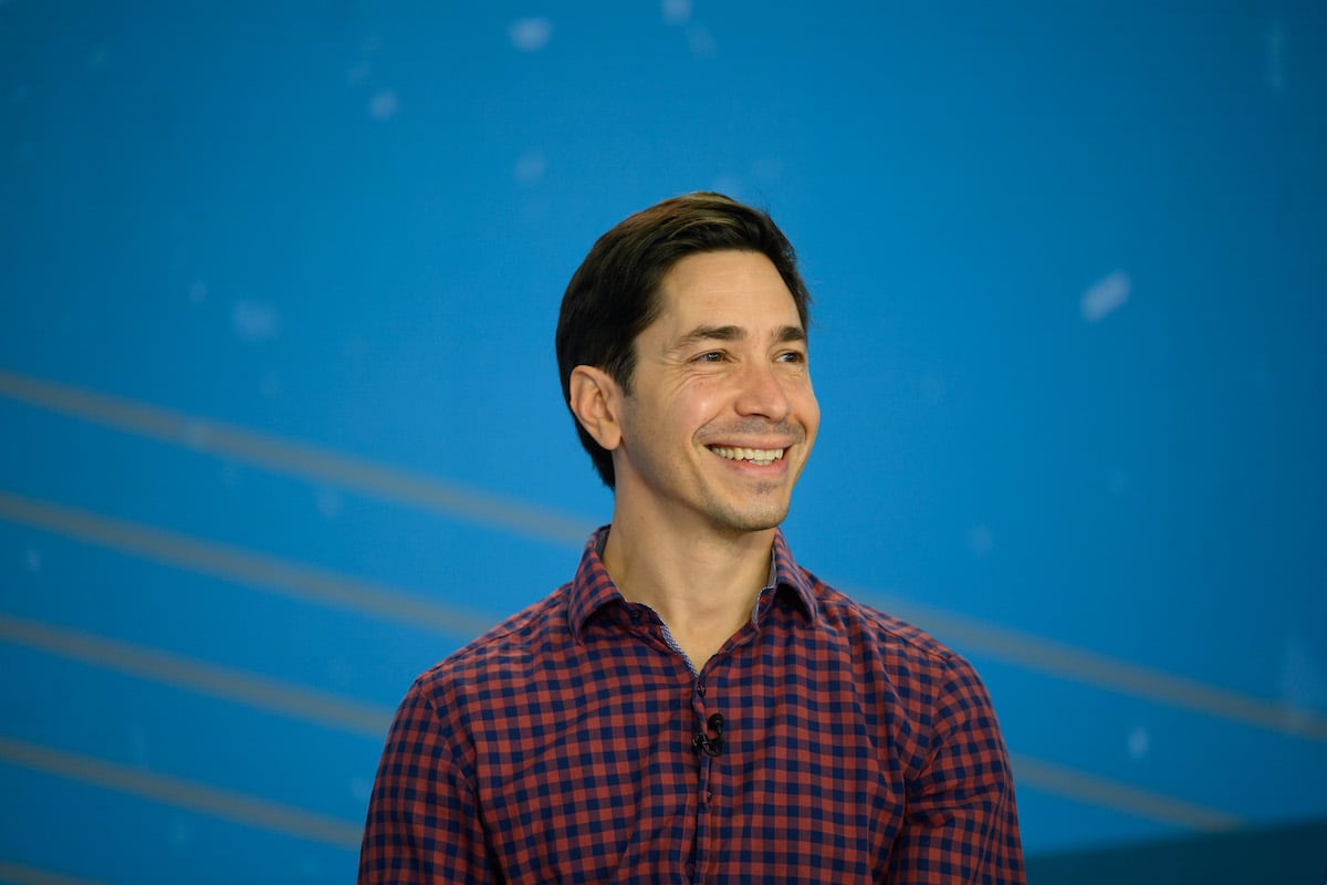 Justin Long smiling in front of a blue background