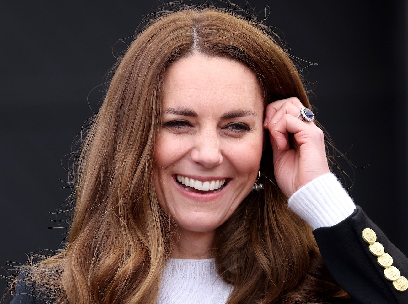 Kate Middleton smiling, one hand touching her hair