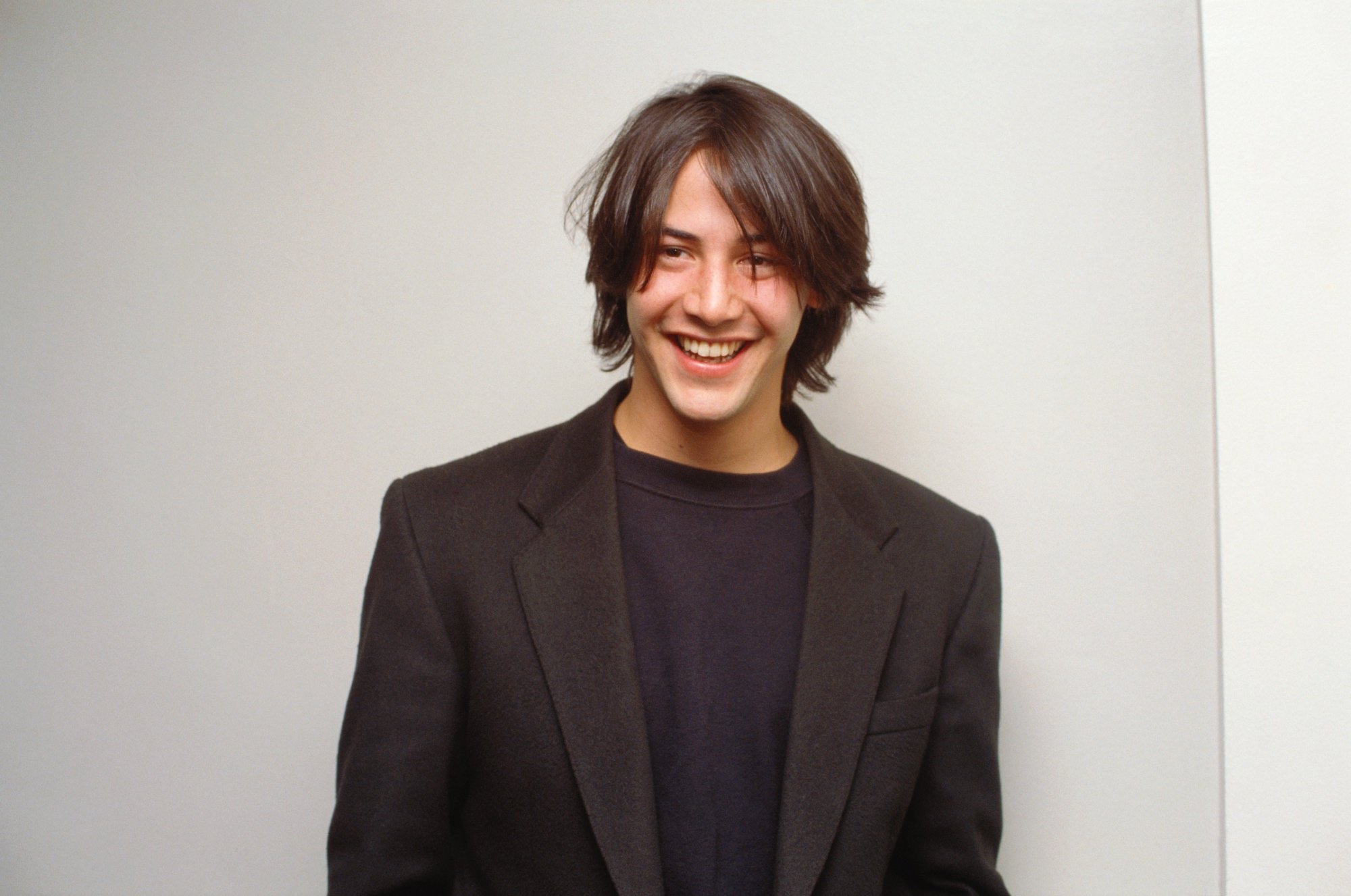 Keanu Reeves smiling in a black blazer and shirt