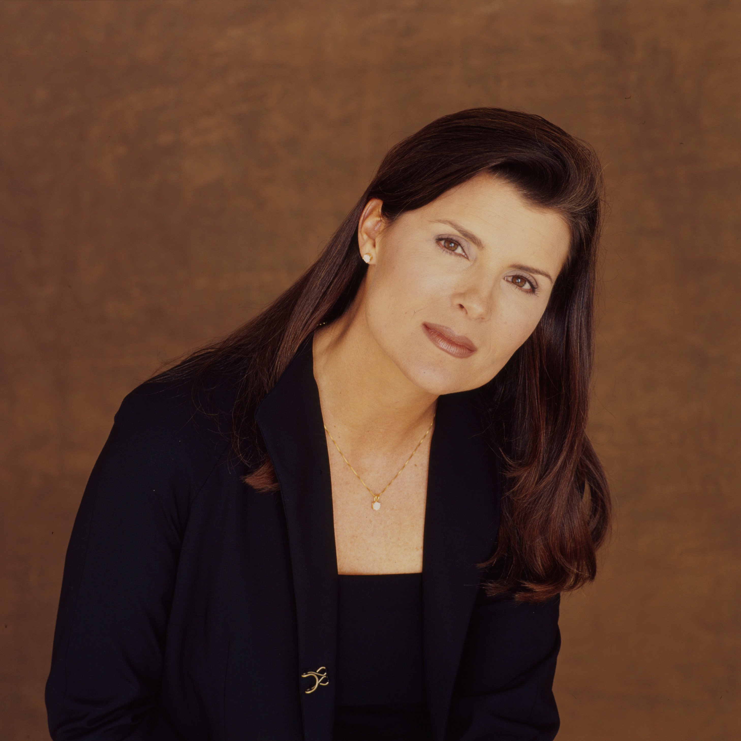 'The Bold and the Beautiful' actor Kimberlin Brown wearing a navy blue pantsuit and standing in front of a brown backdrop.