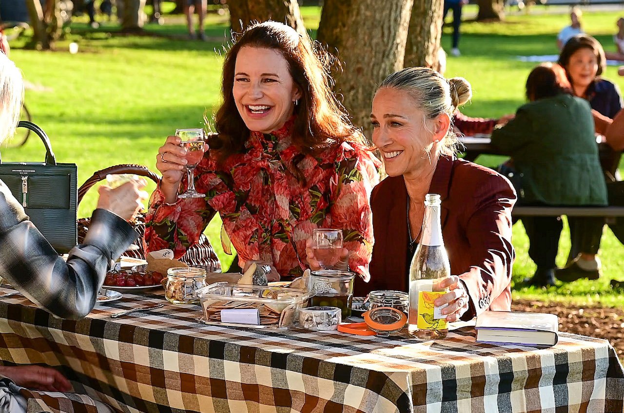 Kristin Davis and Sarah Jessica Parker seen on the set of "And Just Like That..." laughing together at a picnic table in the park.