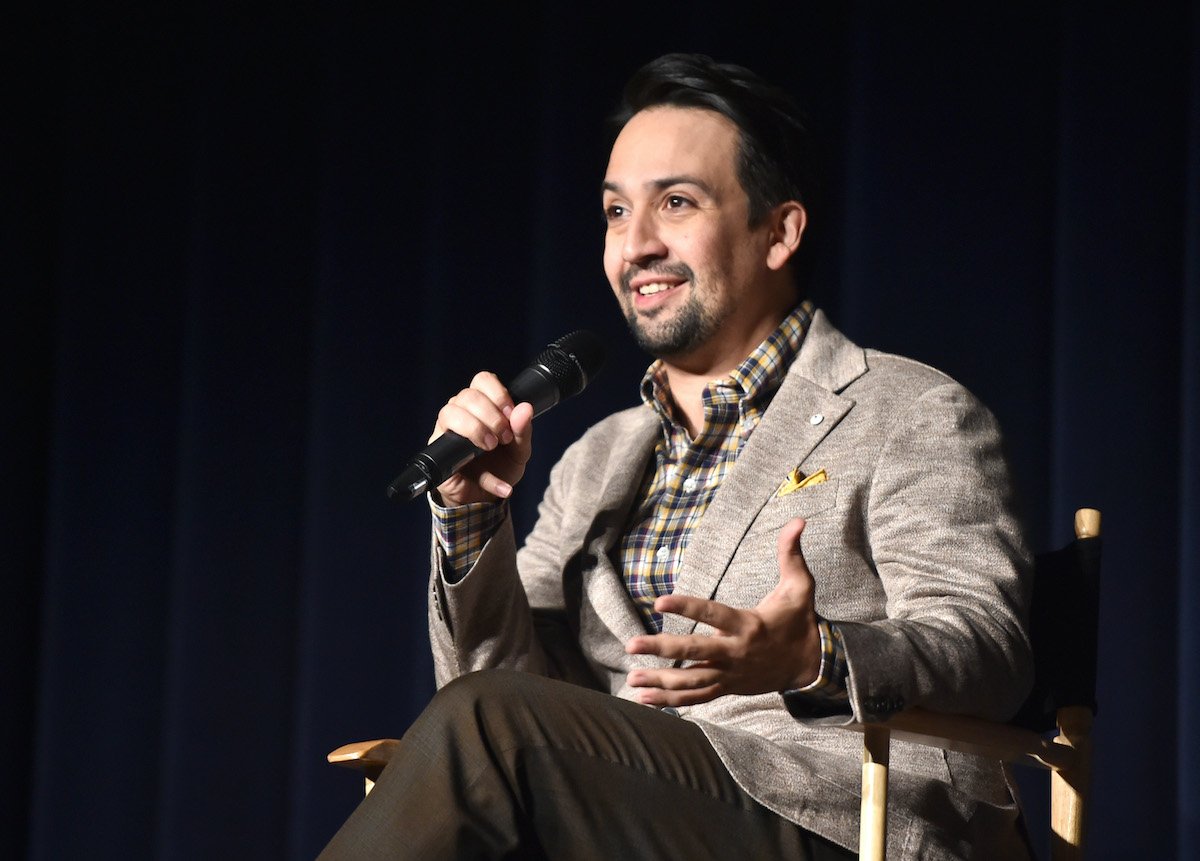 Lin-Manuel Miranda wears a tan jacket and smiles onstage