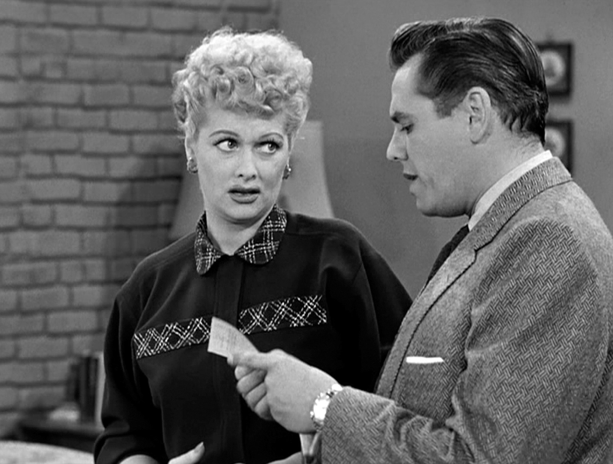 Lucille Ball looks at Desi Arnaz as he reads from a piece of paper. 