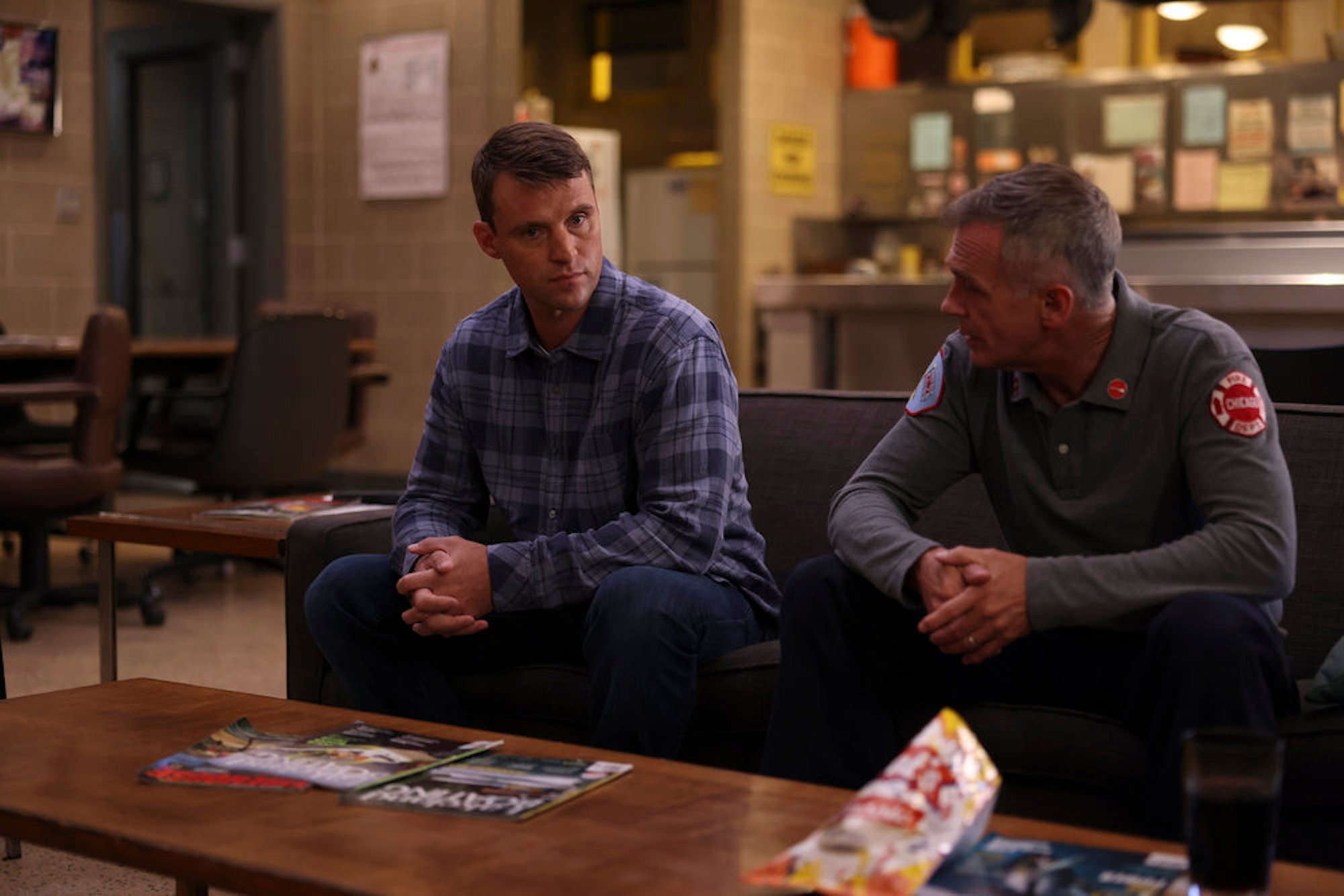 Jesse Spencer as Matthew Casey and David Eigenberg as Christopher Herrmann sitting on a couch together in 'Chicago Fire' Season 10