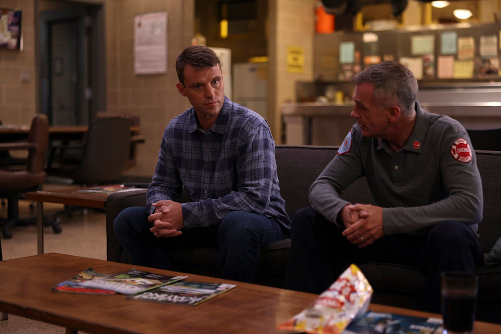Jesse Spencer as Matthew Casey and David Eigenberg as Christopher Herrmann sitting on a couch together in 'Chicago Fire' Season 10 