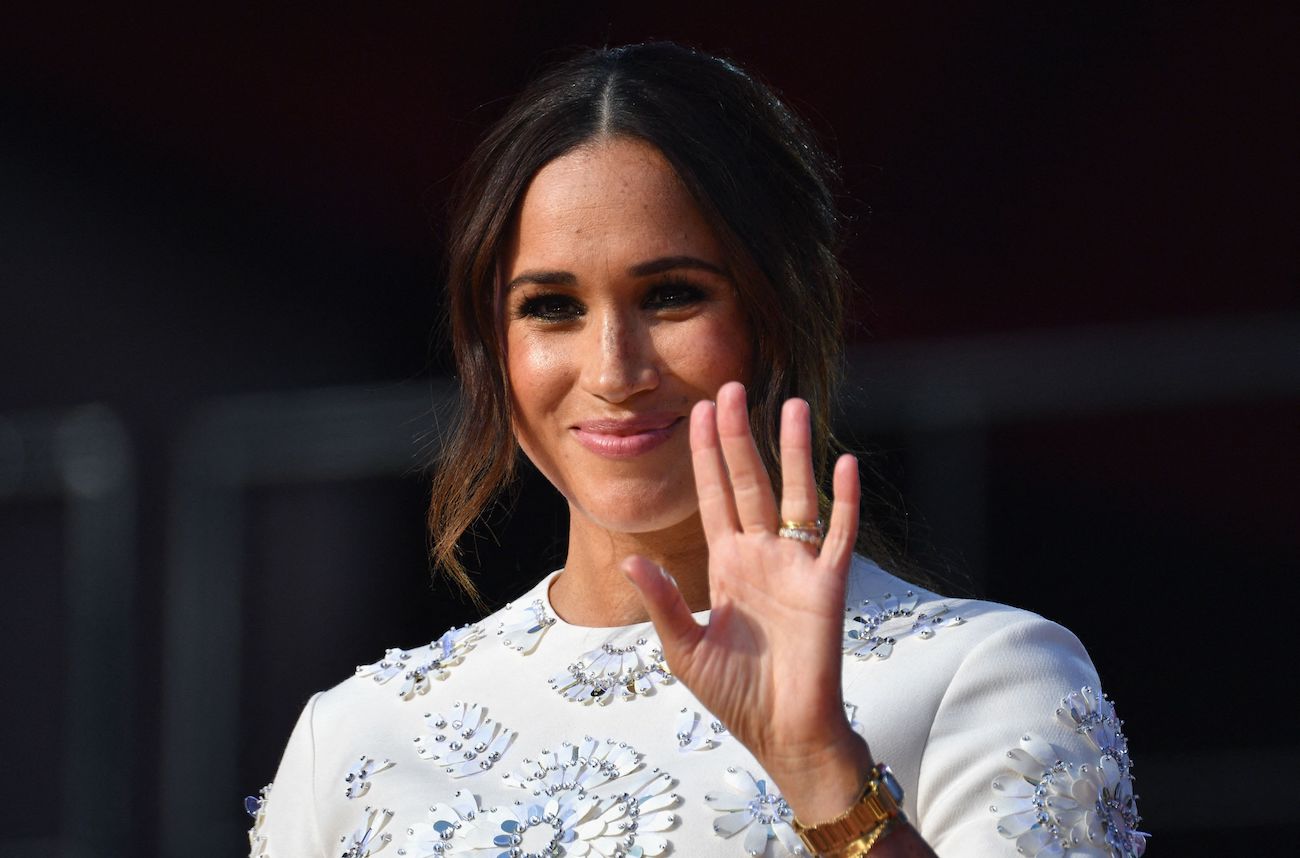 Meghan Markle smiles and waves wearing a white dress