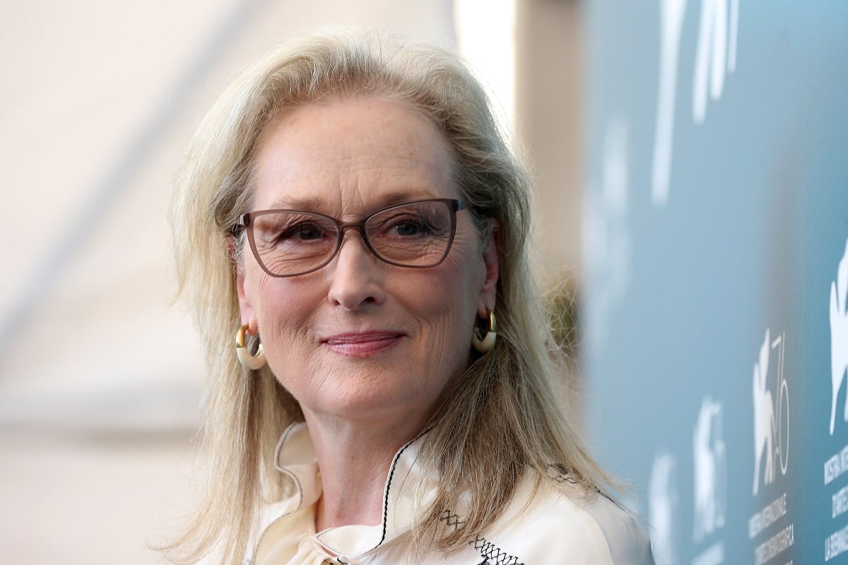 Meryl Streep smirking while wearing glasses and a white dress.