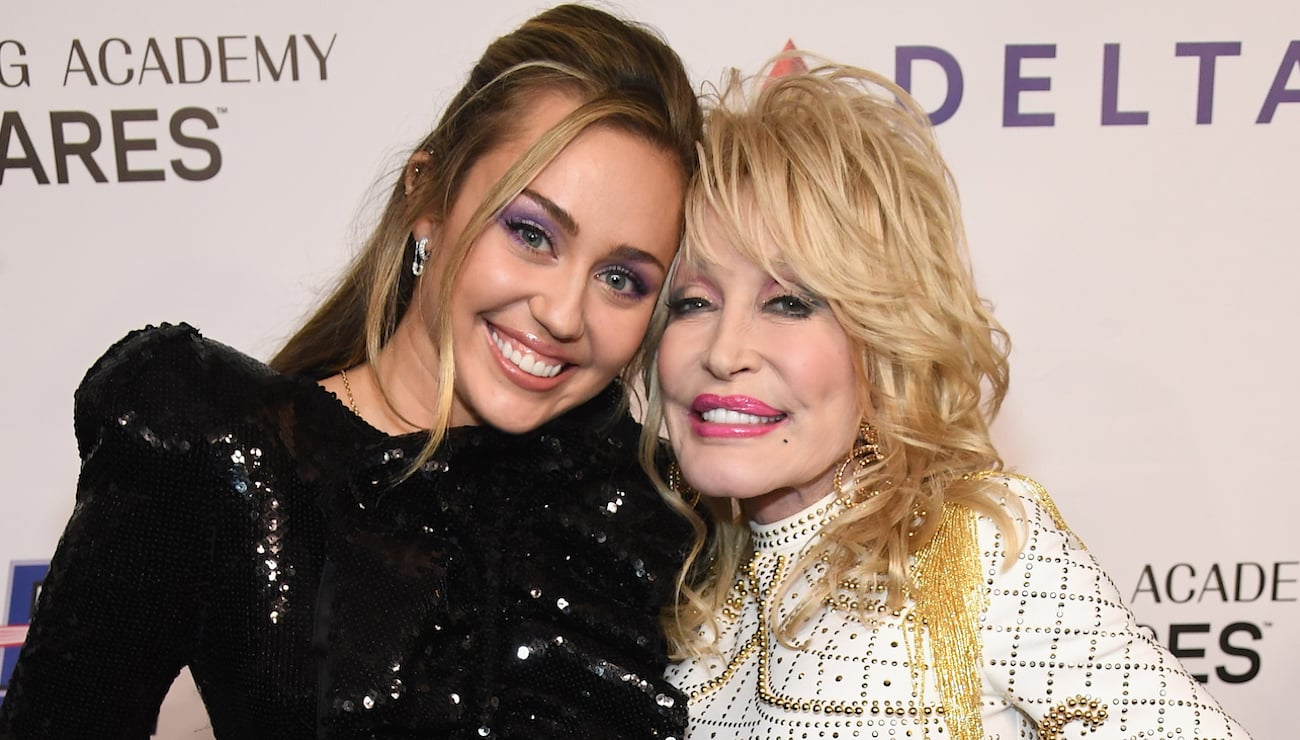 Miley Cyrus wears a black dress as she stands next to Dolly Parton in a white dress