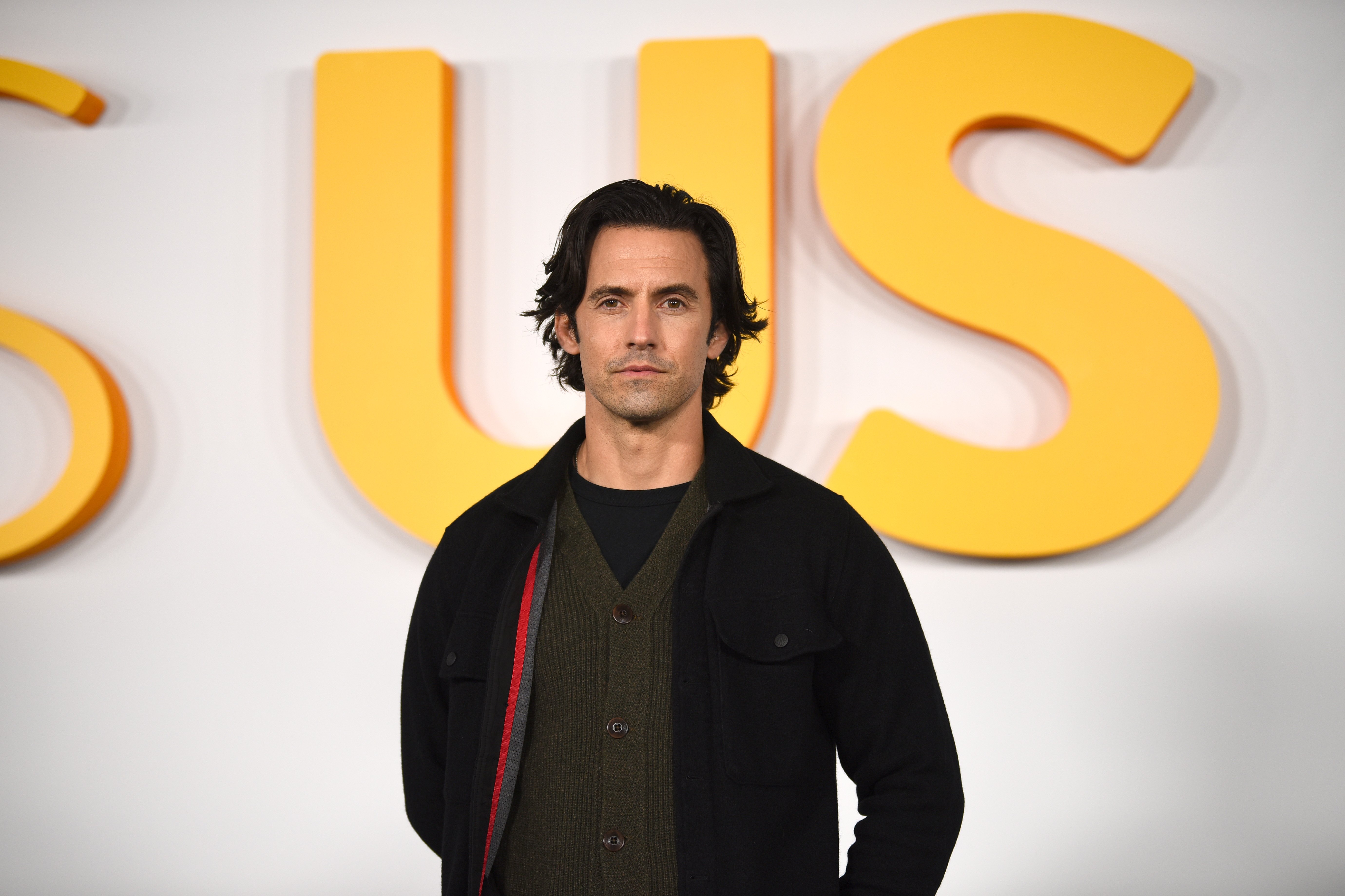 'This Is Us' Season 6 star Milo Ventimiglia, who plays Jack Pearson, wears a black jacket over a green cardigan over a black shirt.