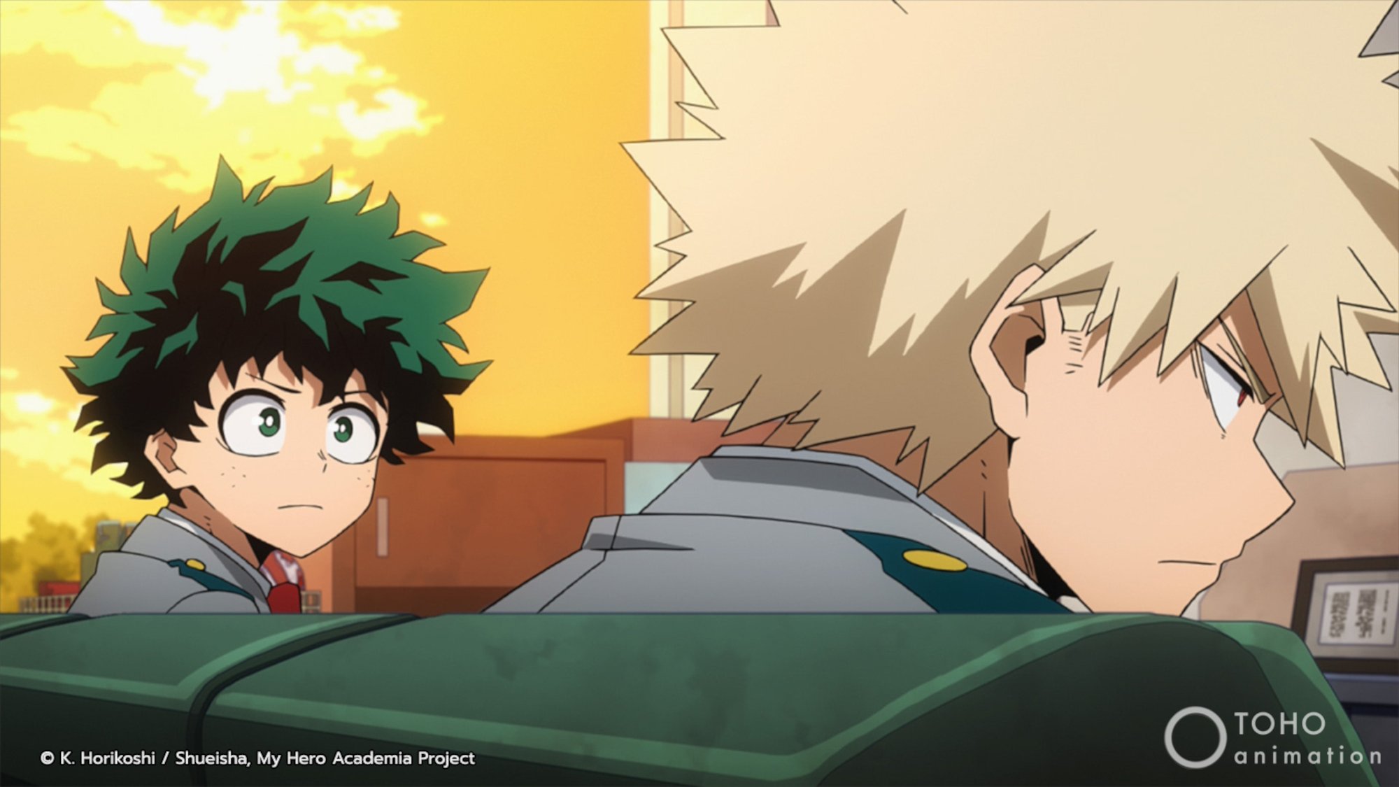 Deku and Bakugo in 'My Hero Academia' Season 5. Deku is staring at Bakugo, who is sitting next to him on a couch.