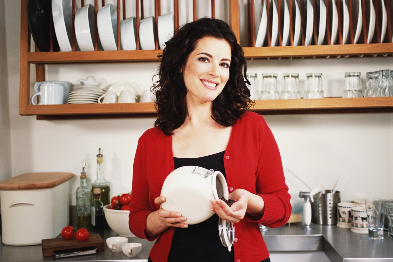 Nigella Lawson smiles wearing a red cardigan while holding a container