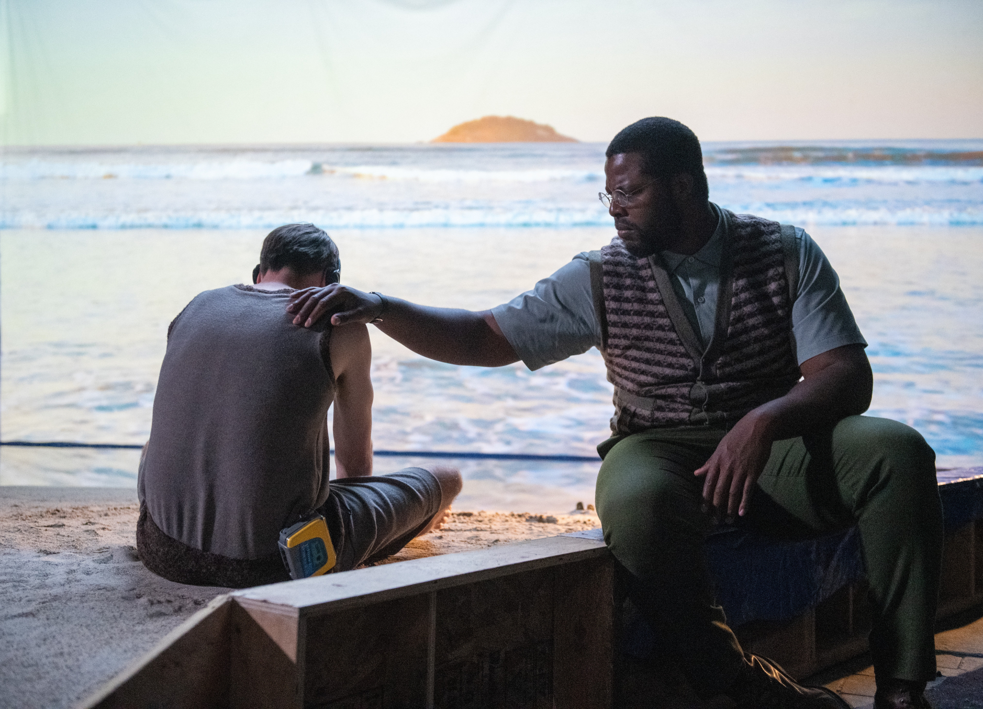'Nine Day's David Rysdahl as Mike and Winston Duke as Will sitting on the beach comforting Mike