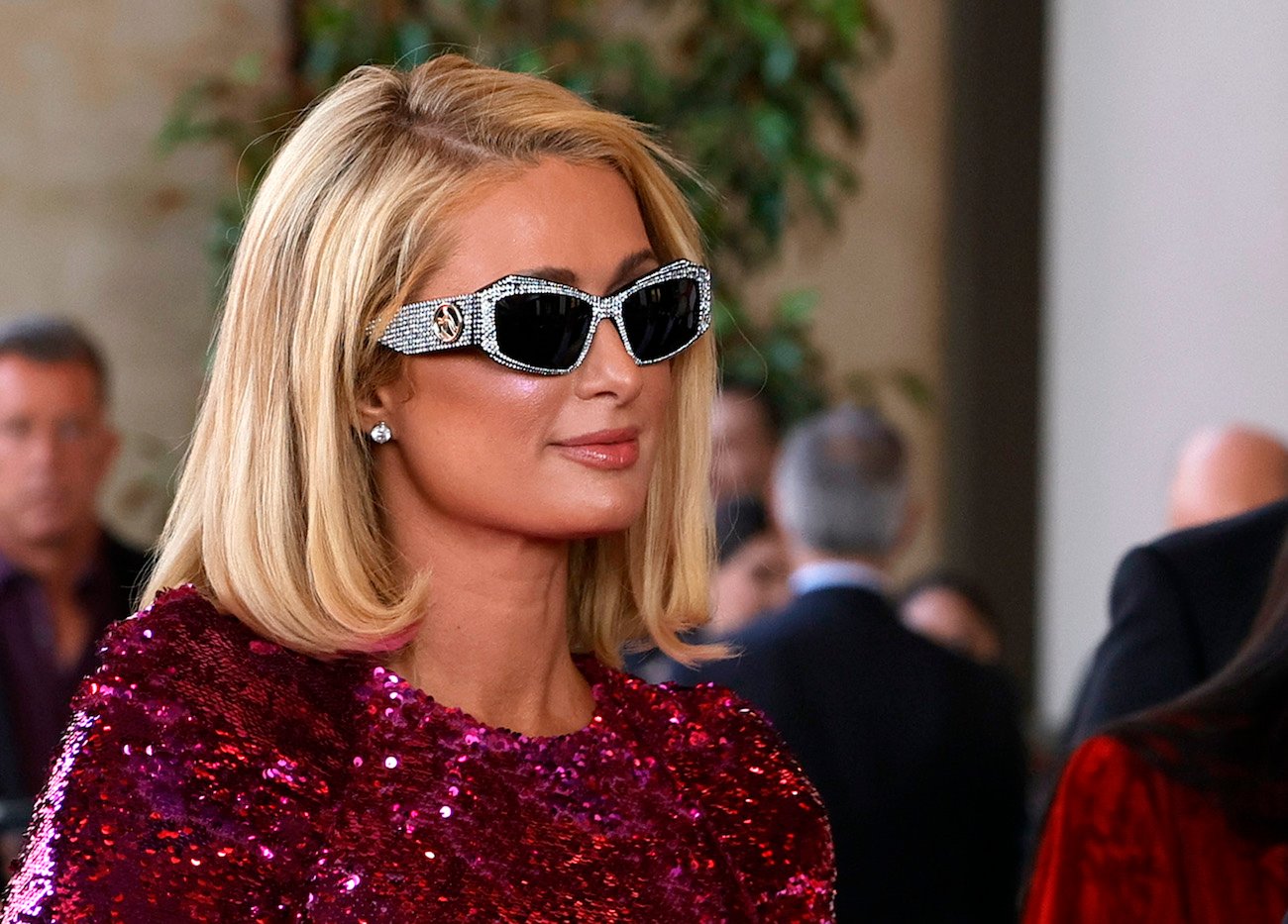 Paris Hilton smiles wearing sunglasses and a pink sequin dress